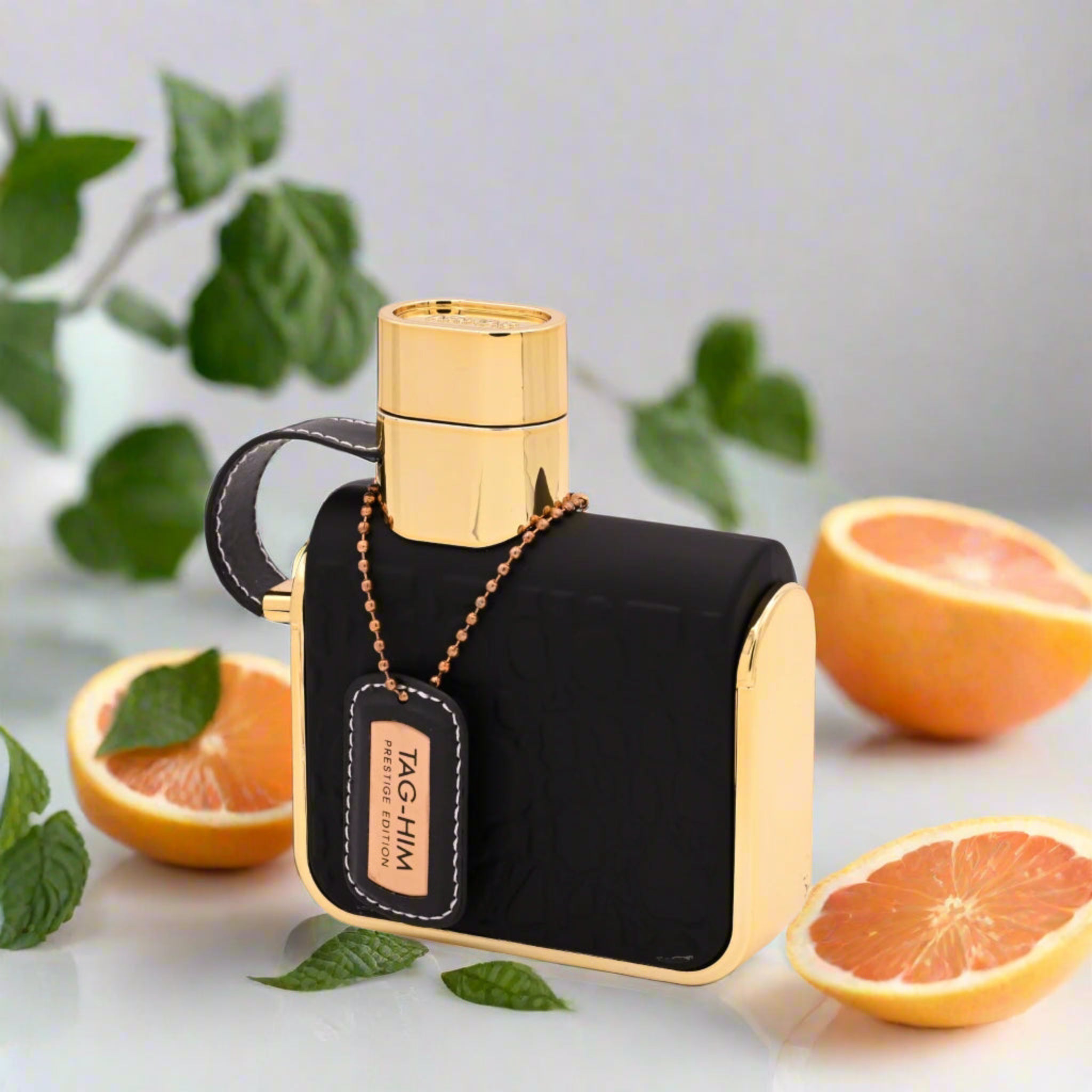 Black and gold perfume bottle with oranges and leaves on a light background