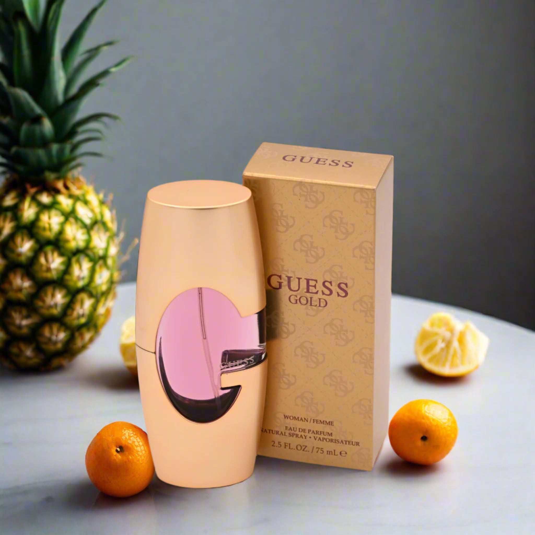 Guess Gold perfume bottle and packaging with fruits on a gray surface