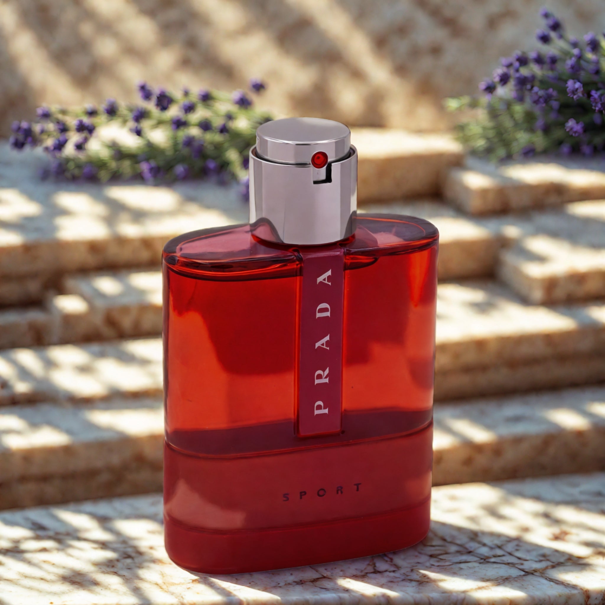 Red Prada perfume bottle on a stone surface with flowers in the background
