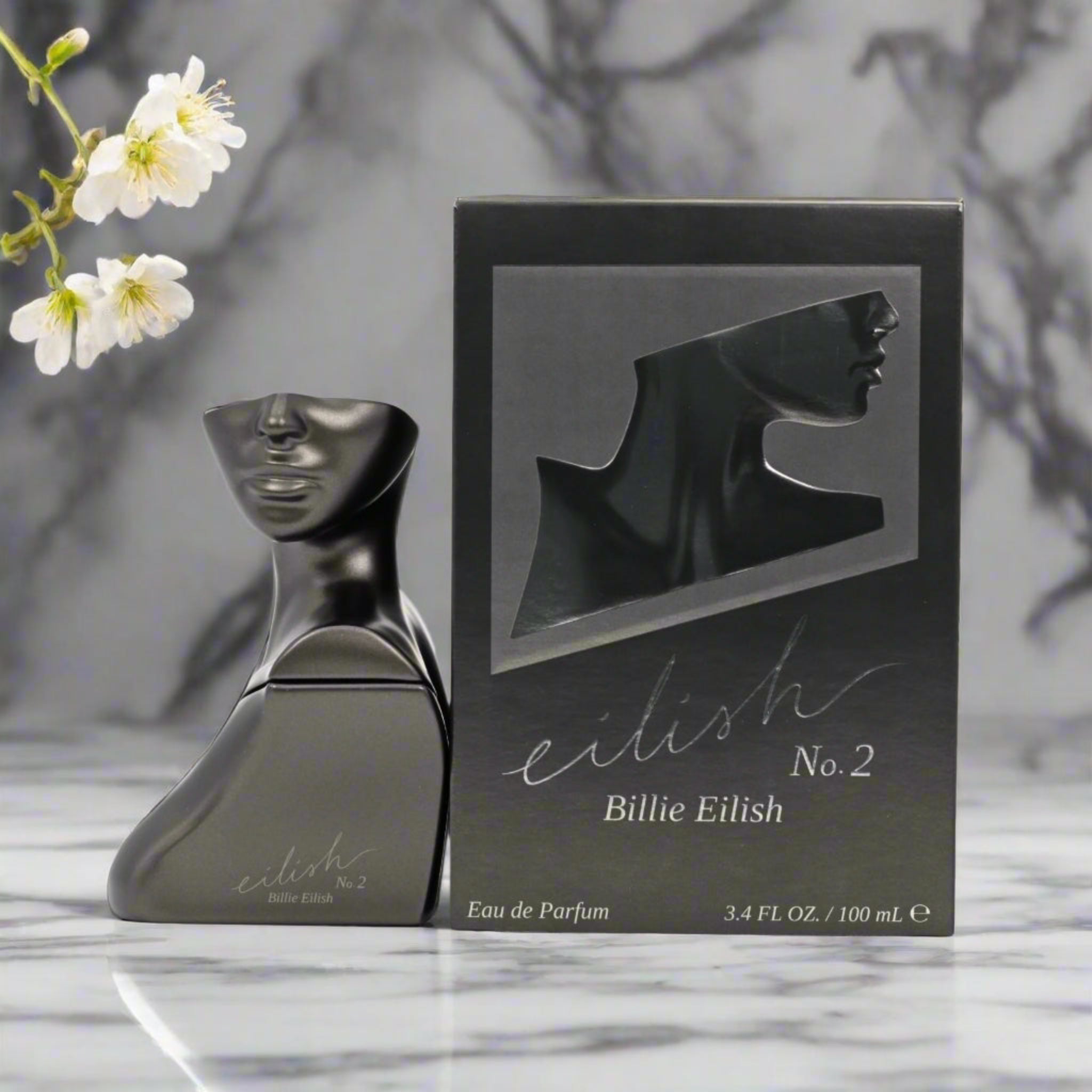 Black 'Billie Eilish' perfume bottle and packaging on a marble surface with flowers.
