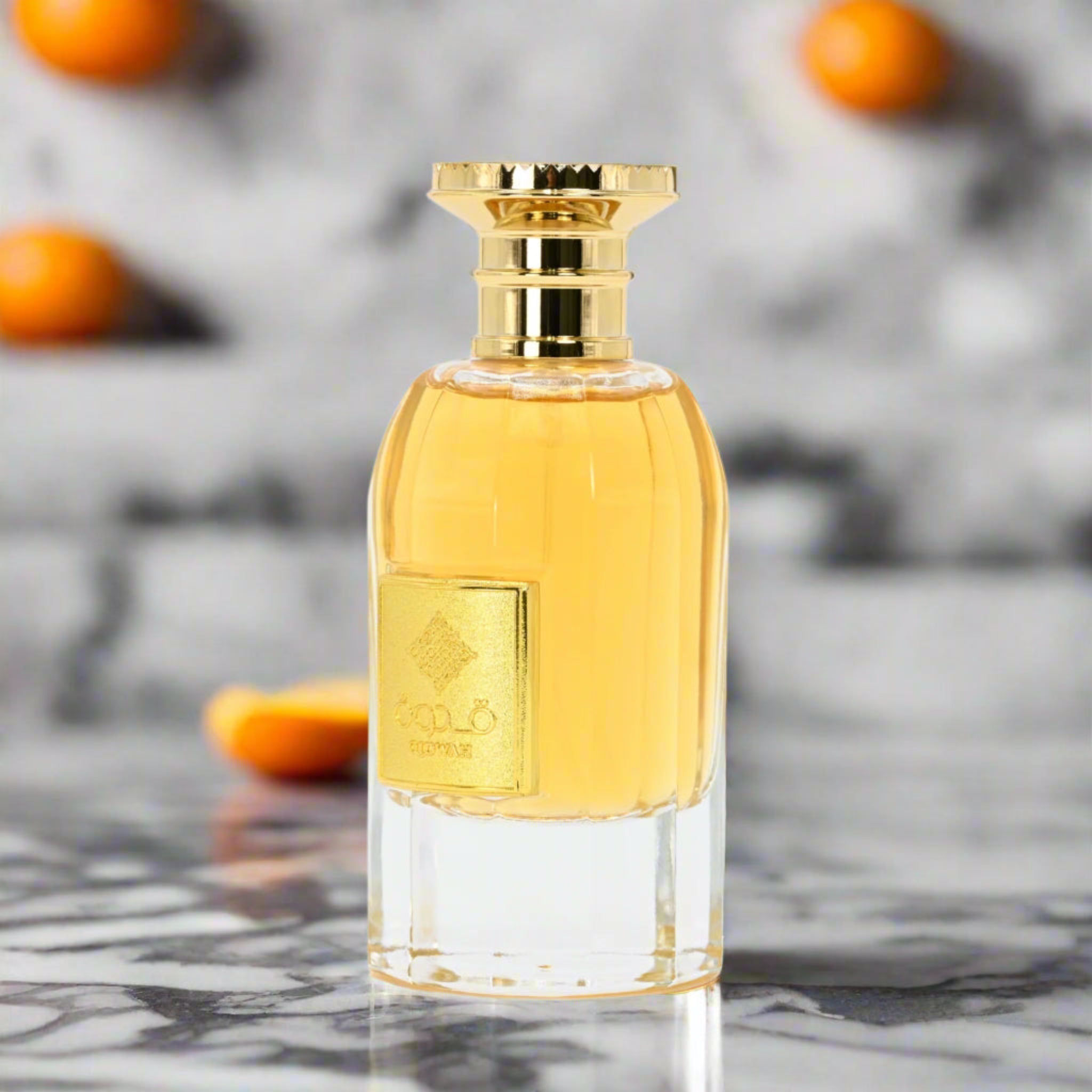 Perfume bottle with gold cap on a marble surface with blurred oranges in the background