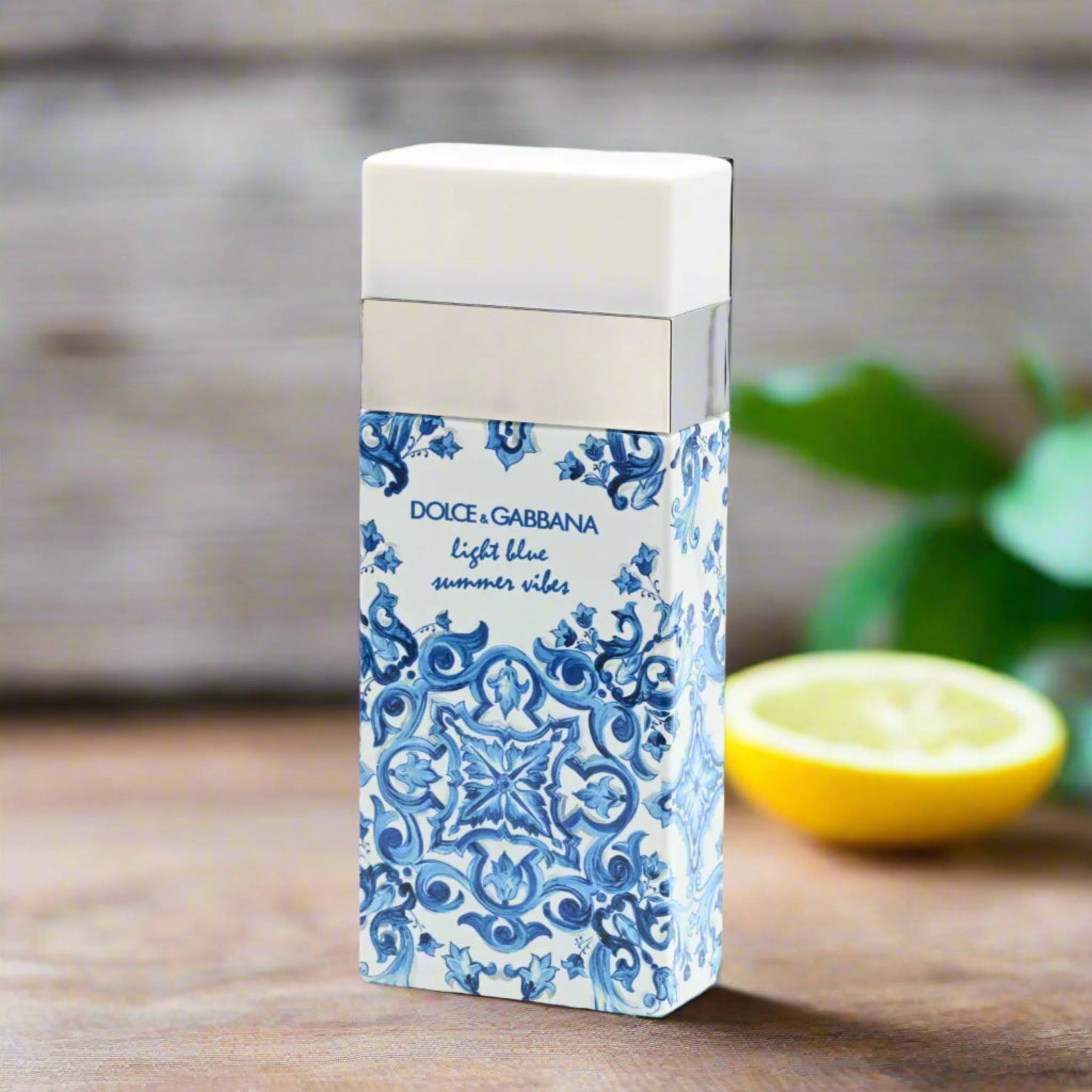 Dolce & Gabbana perfume packaging with blue and white design on a wooden surface with a lemon and green leaves.