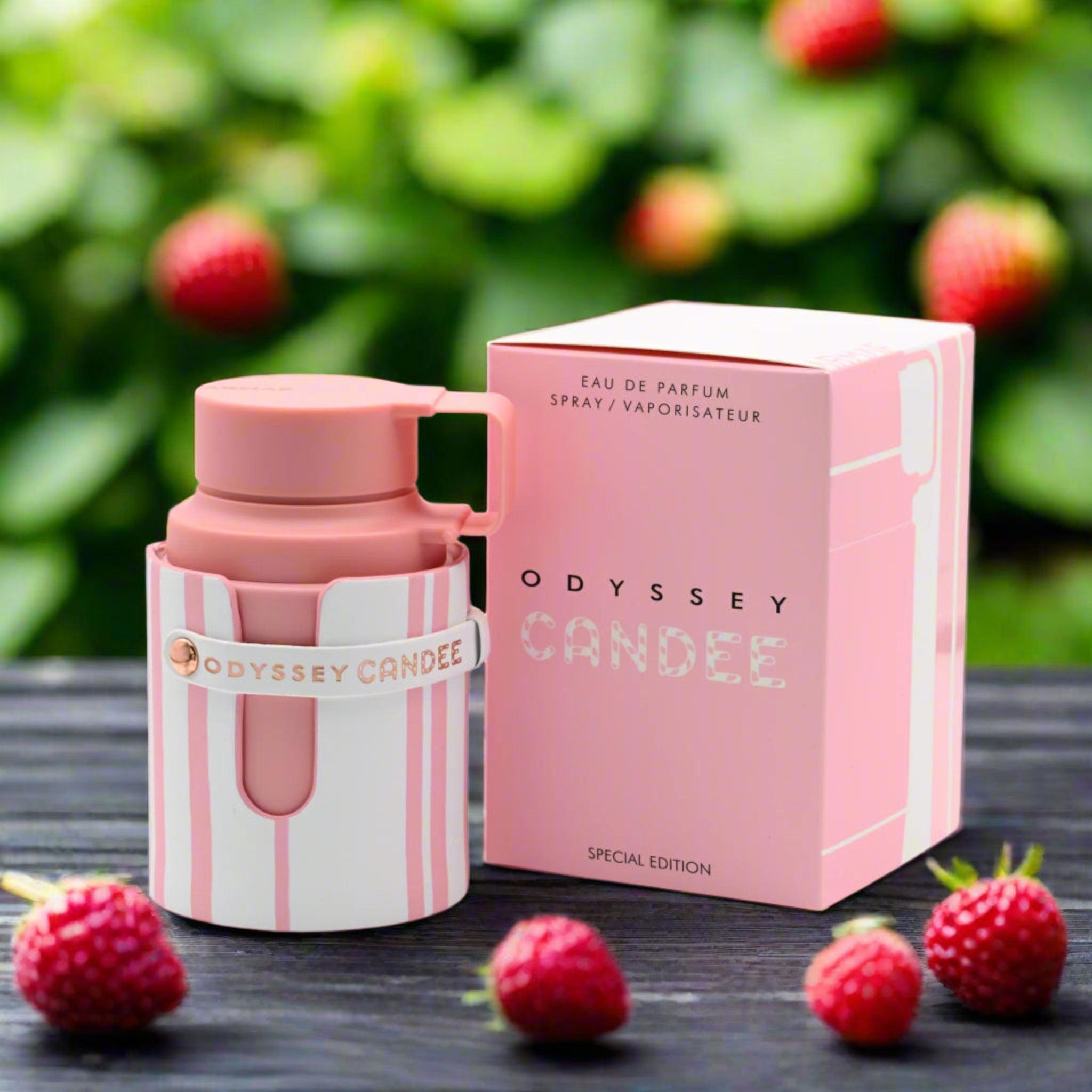Pink and white_ODYSSEY CANDEE perfume bottle and packaging with raspberries on a wooden surface.