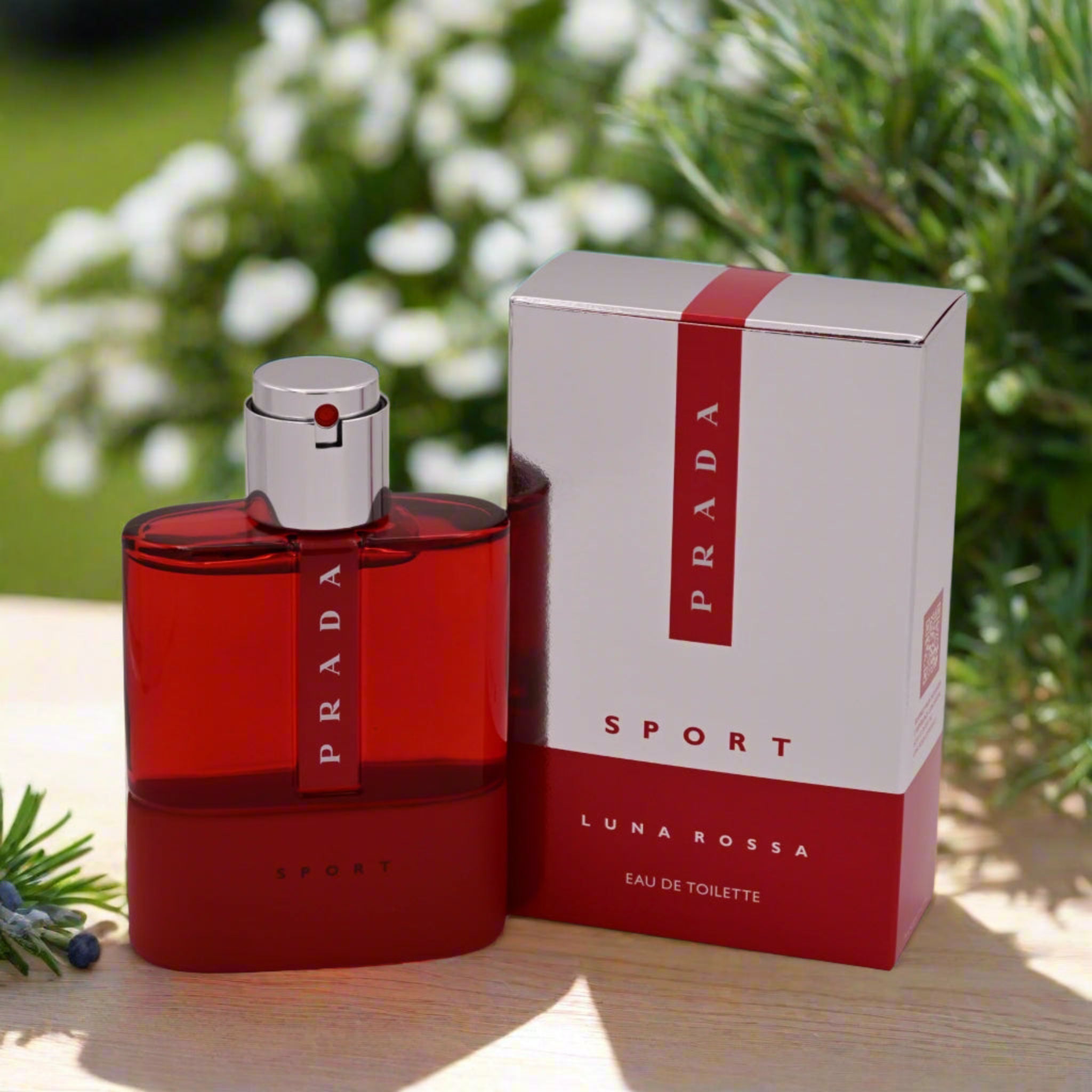 Red Prada Luna Rossa perfume bottle and packaging on a wooden surface with greenery in the background