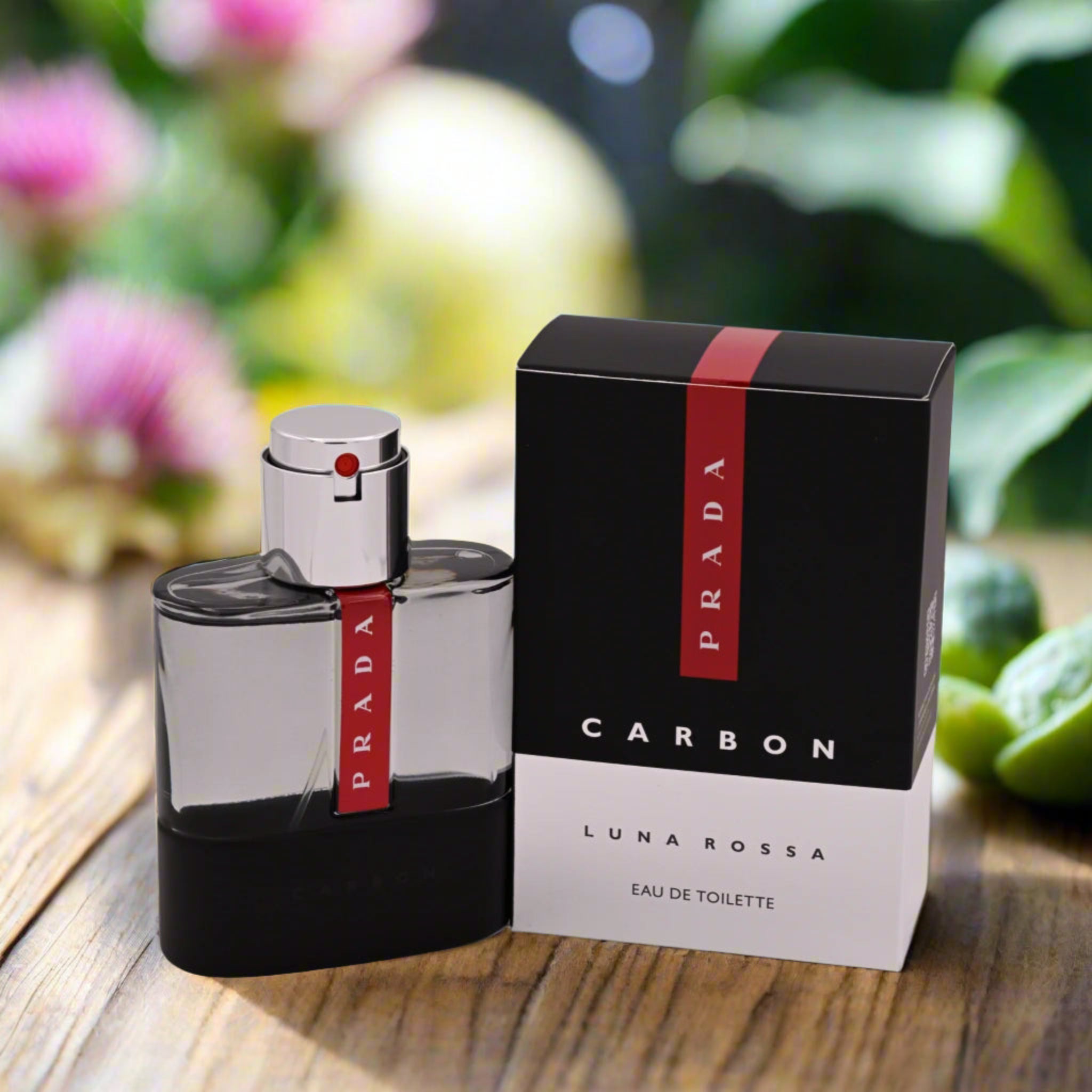 Prada Luna Rossa perfume bottle and packaging on a wooden surface with blurred flowers and plants in the background