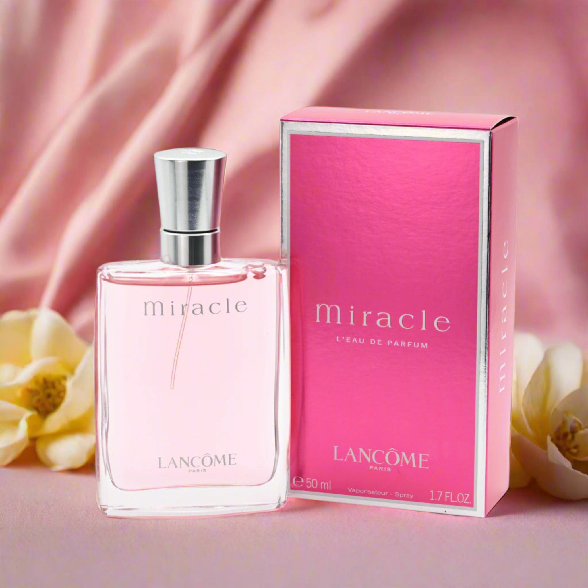 Lancome Miracle perfume bottle and packaging on a pink background with flowers.