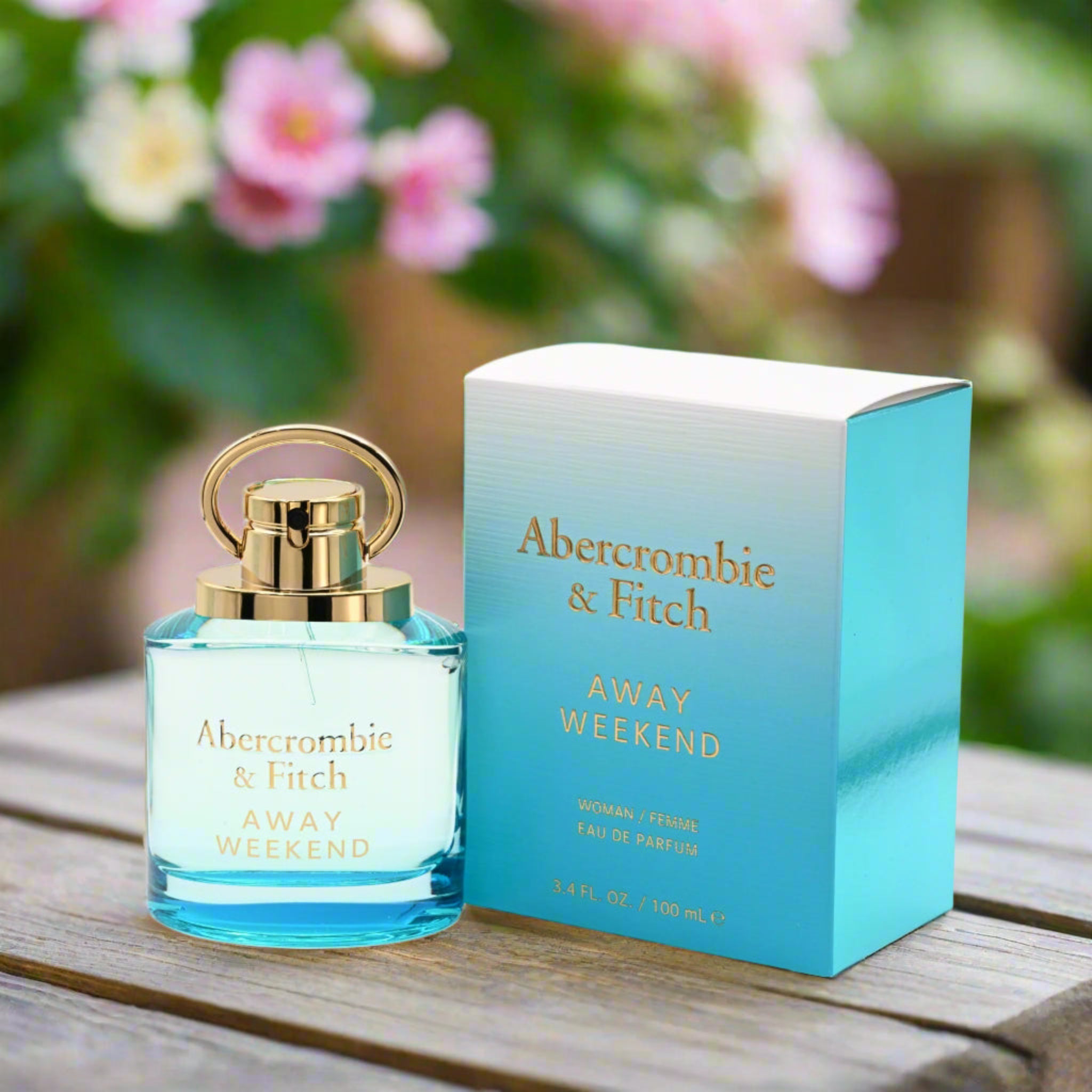 Abercrombie & Fitch Away Weekend perfume bottle and packaging on a wooden surface with flowers in the background