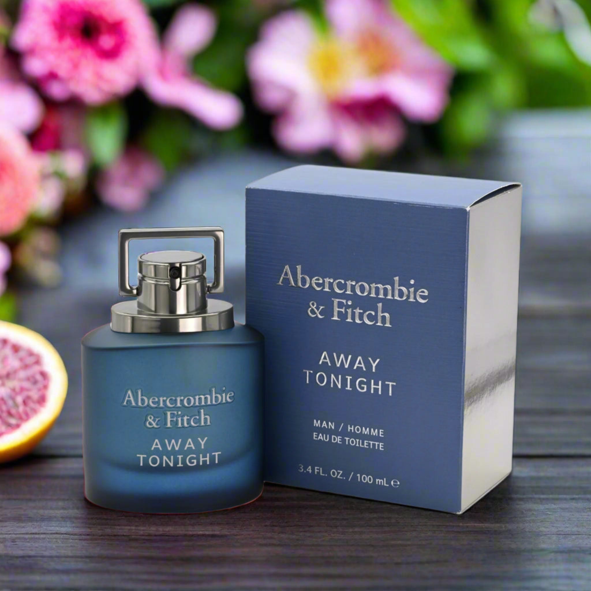 Abercrombie & Fitch Away Tonight perfume bottle and packaging on a wooden surface with flowers in the background.