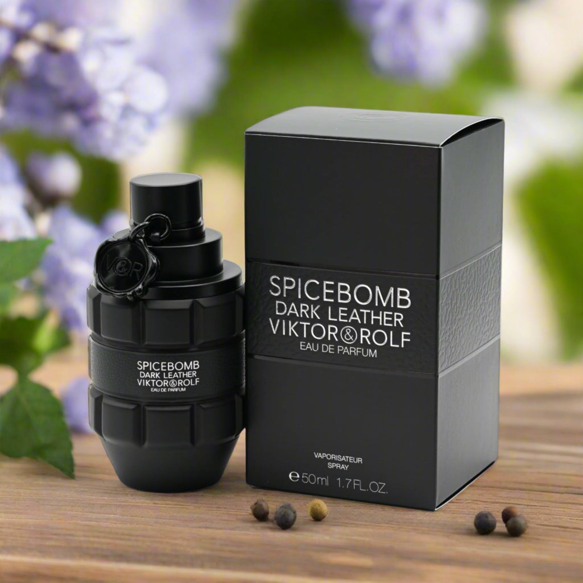 Spicebomb Dark Leather Viktor & Rolf perfume bottle and packaging on a wooden surface with blurred flowers in the background.