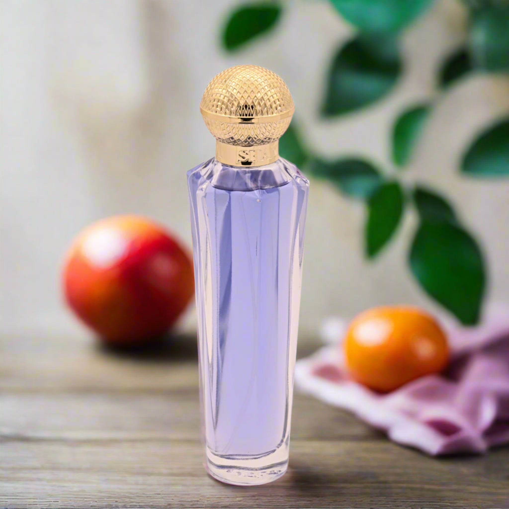Perfume bottle with decorative cap on a wooden surface with fruits and leaves in the background