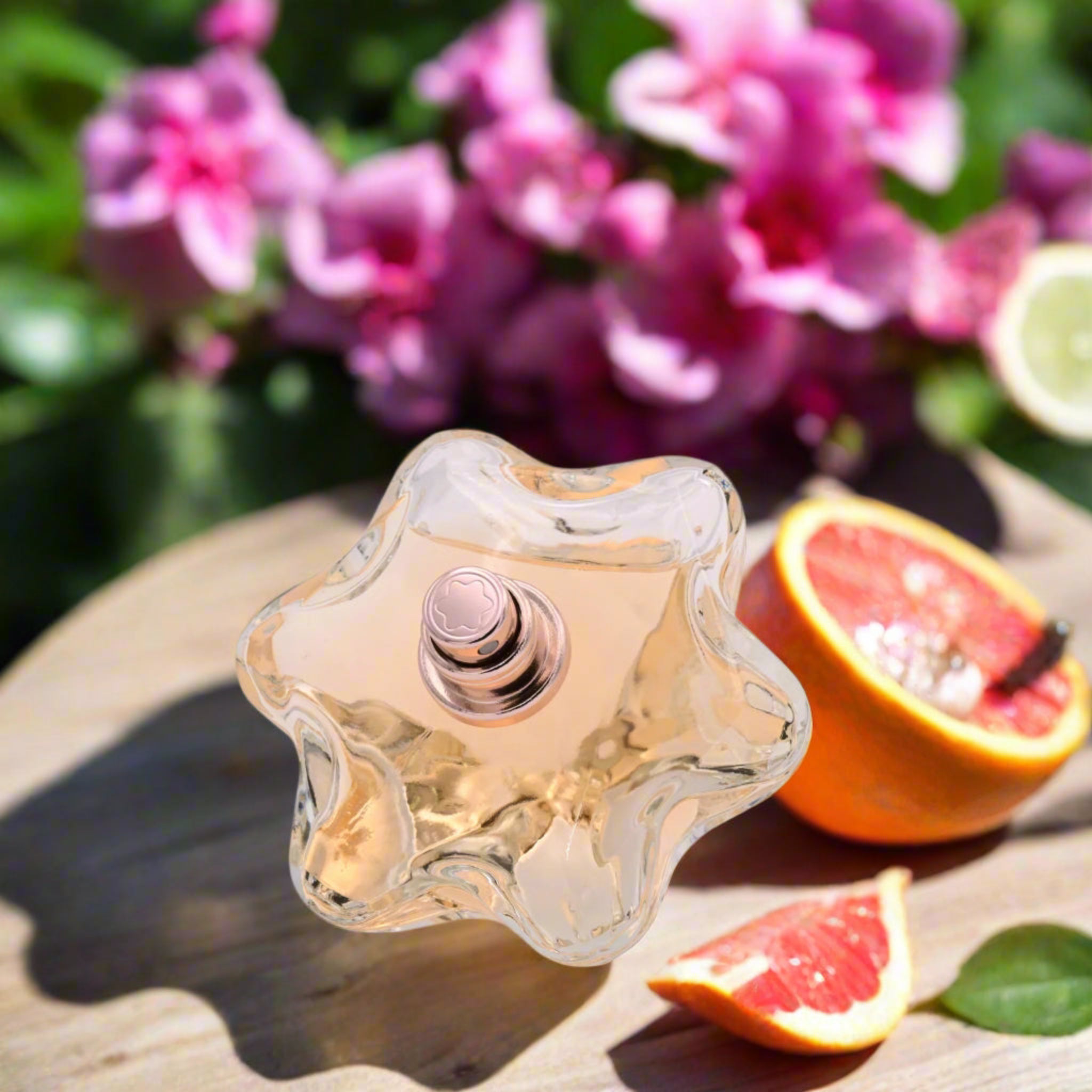Star-shaped perfume bottle with pink flowers and sliced oranges on a wooden surface