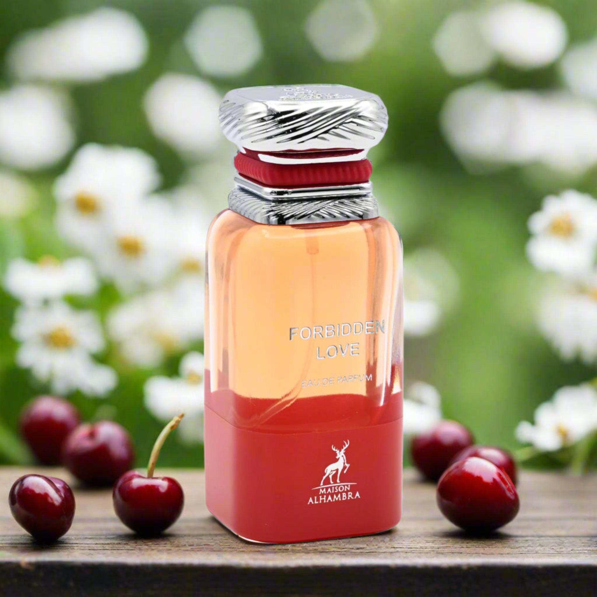 Perfume bottle labeled 'Forbidden Love' by Maison Alhambra with cherries on a wooden surface and floral background.