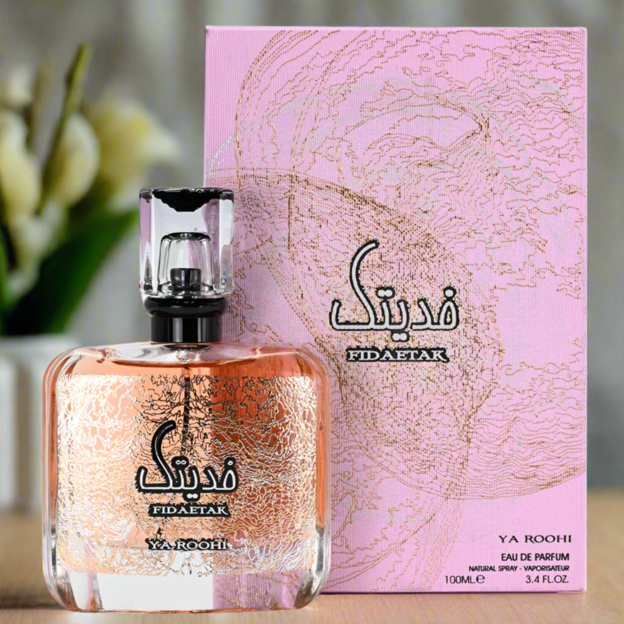 Fidaetak Ya Roohi perfume bottle and packaging on a table with flowers in the background