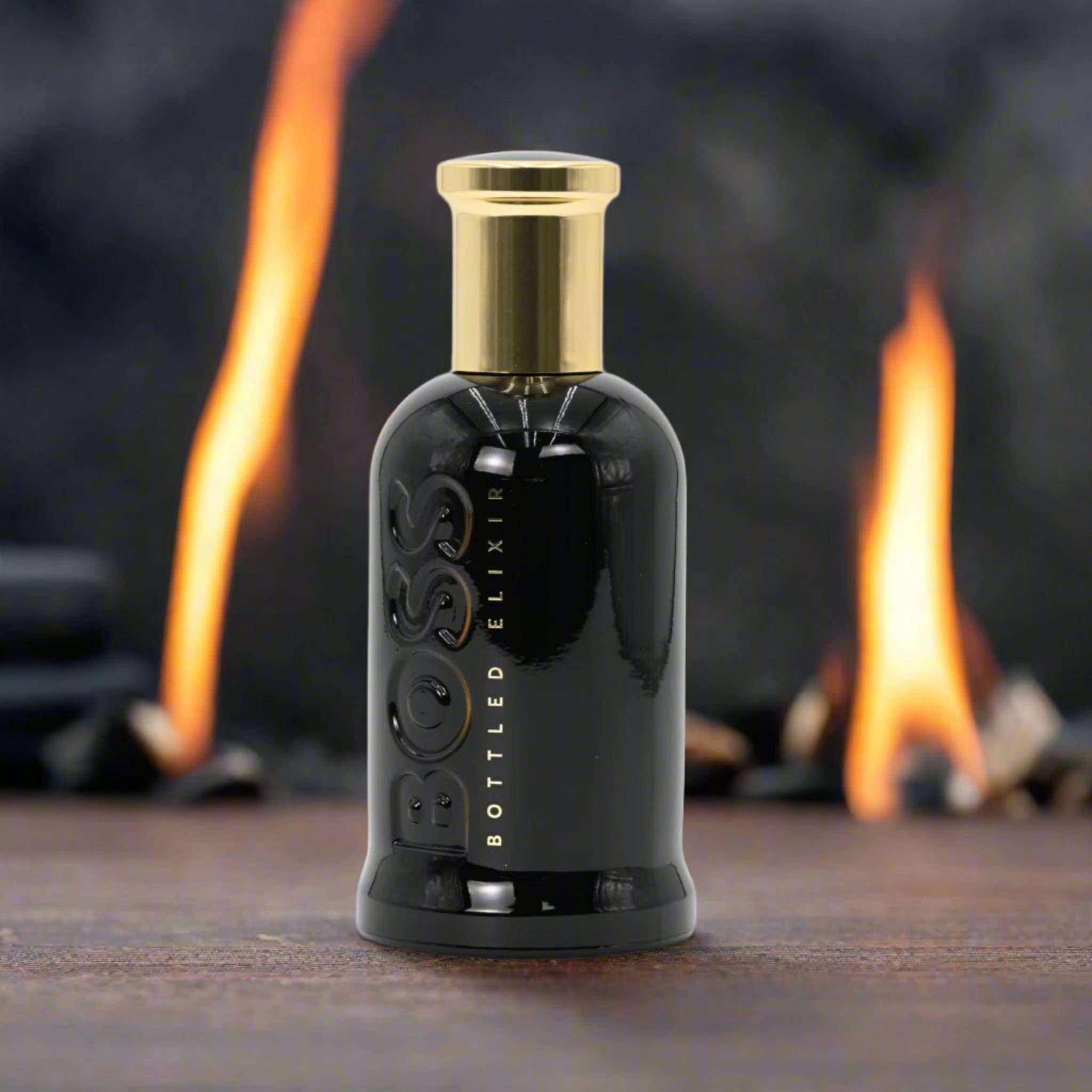 BOSS Bottled Elixir perfume bottle with a gold cap on a wooden surface with a blurred background of flames.