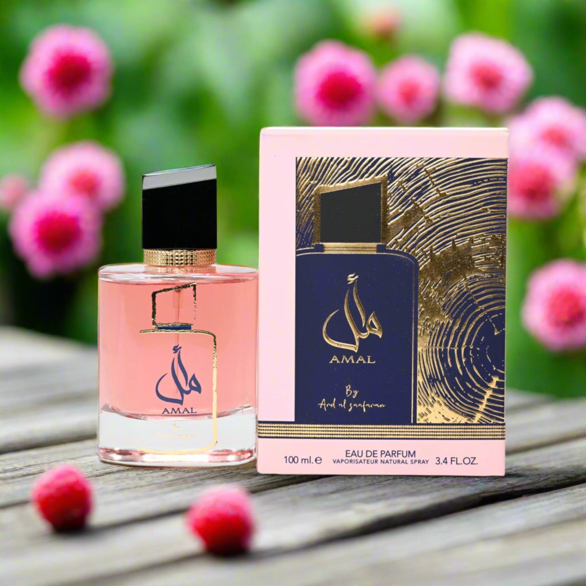 AMAL perfume bottle and packaging on a wooden surface with pink flowers in the background