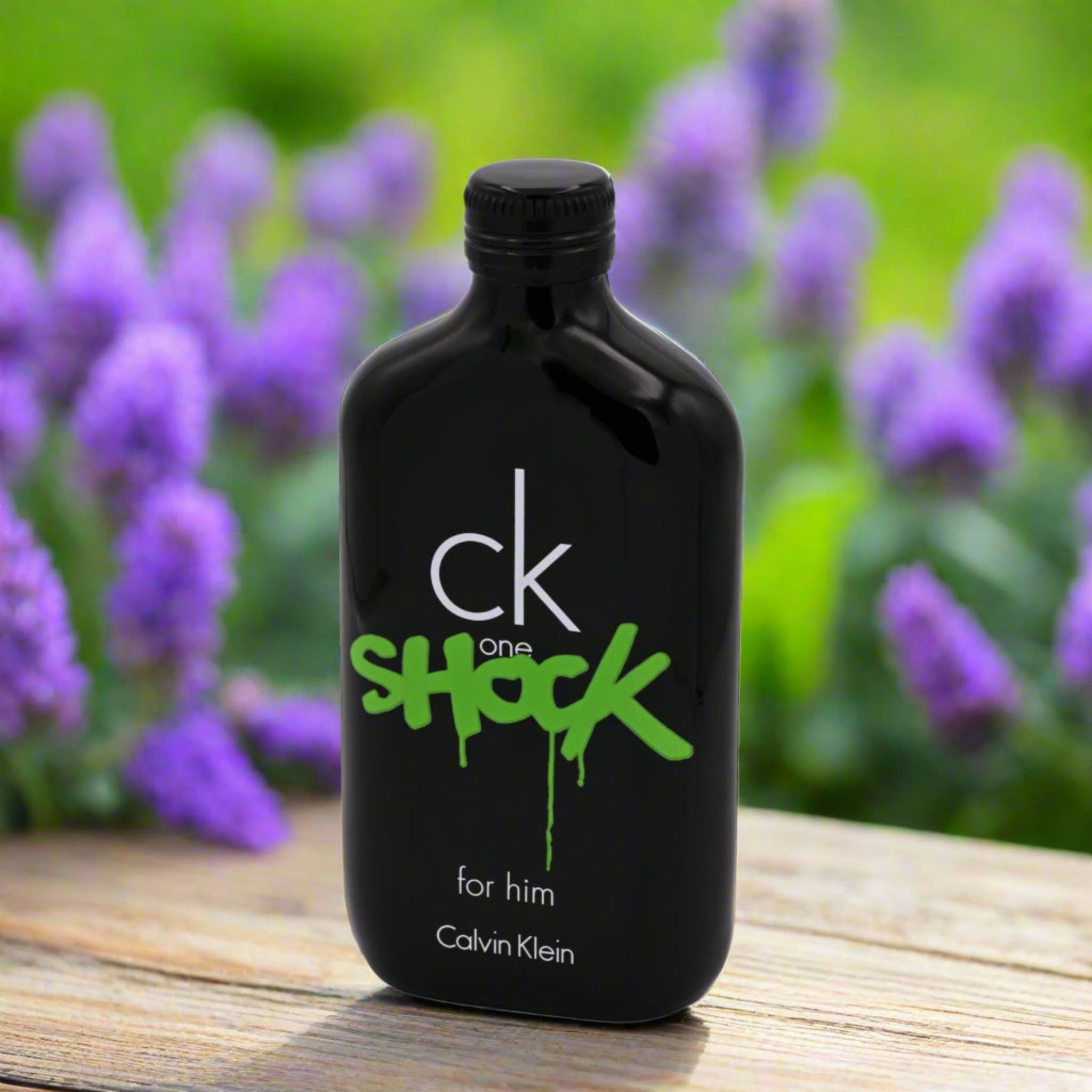 Black bottle of Calvin Klein 'ck one shock' cologne with purple flowers in the background