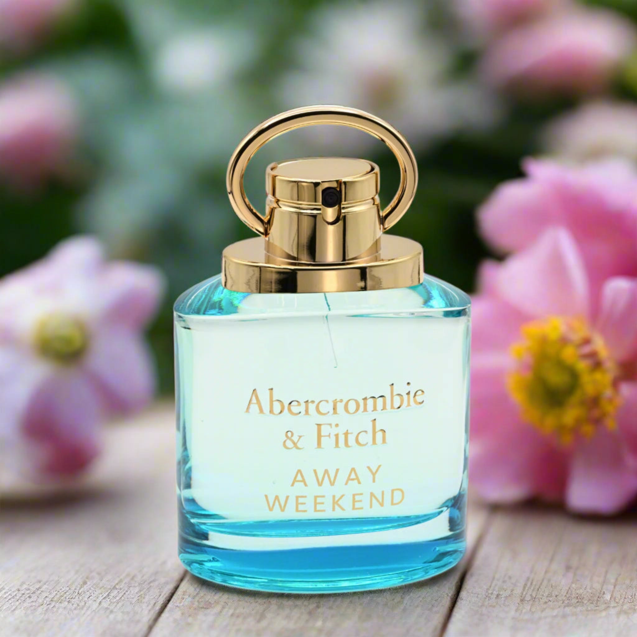 Perfume bottle with gold cap on a wooden surface with flowers in the background