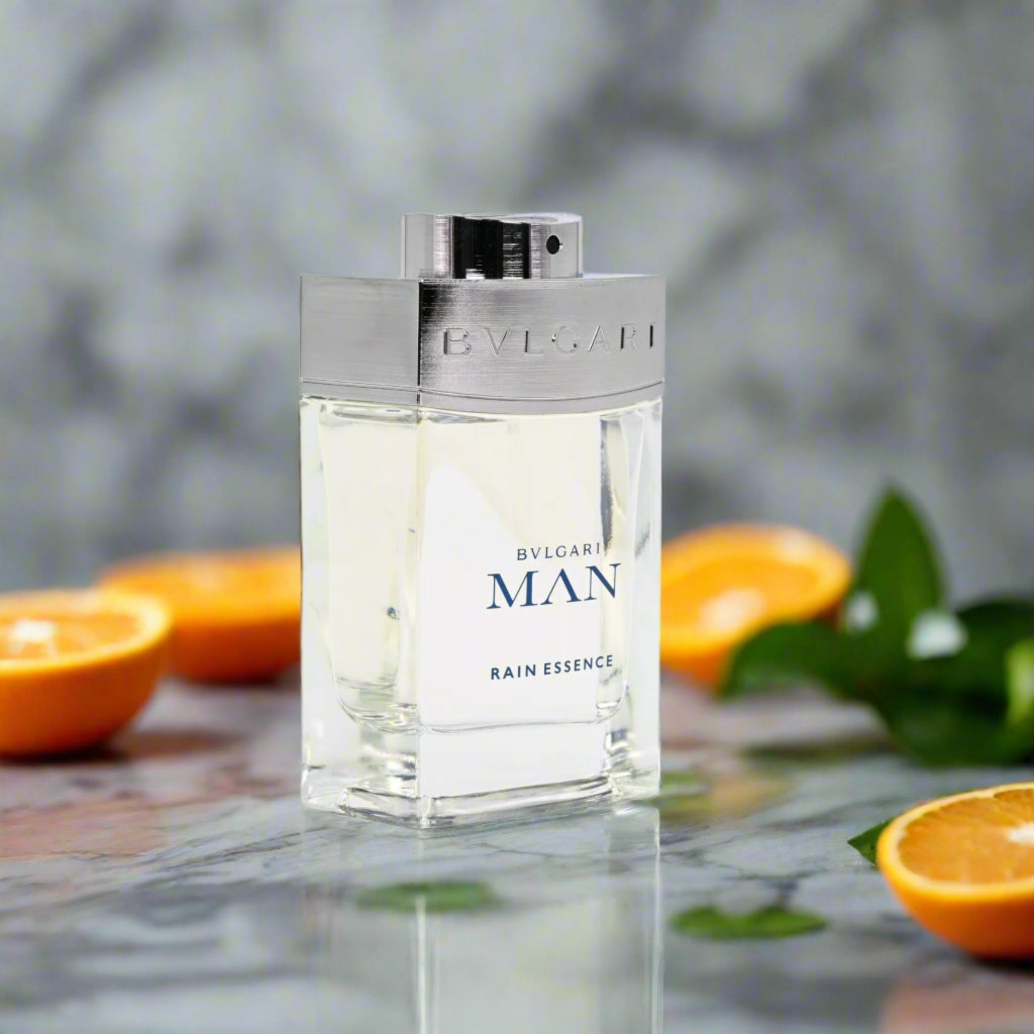 Bvlgari Man Rain Essence perfume bottle with oranges and leaves on a reflective surface