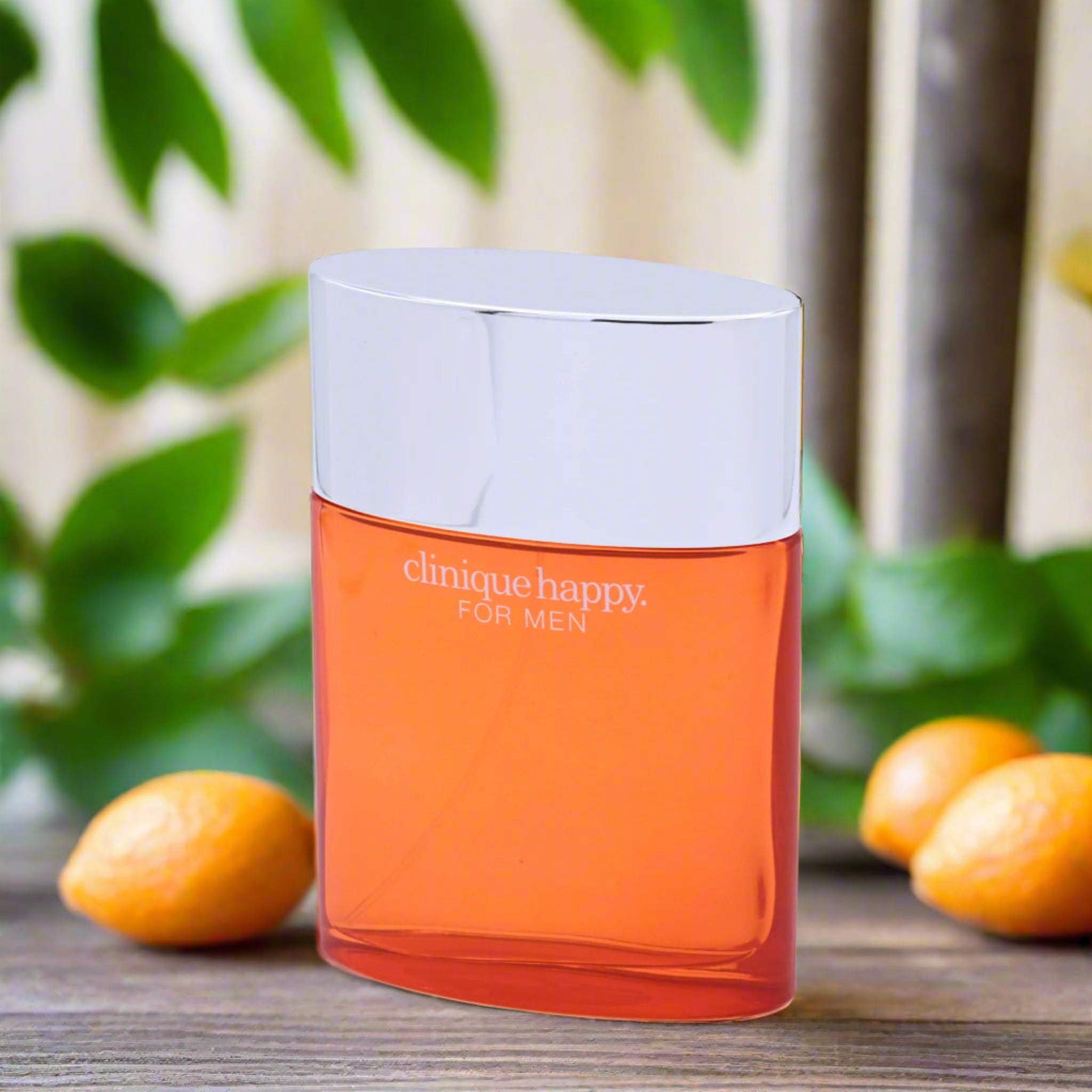 Orange Clinique Happy for Men perfume bottle with green leaves and oranges in the background