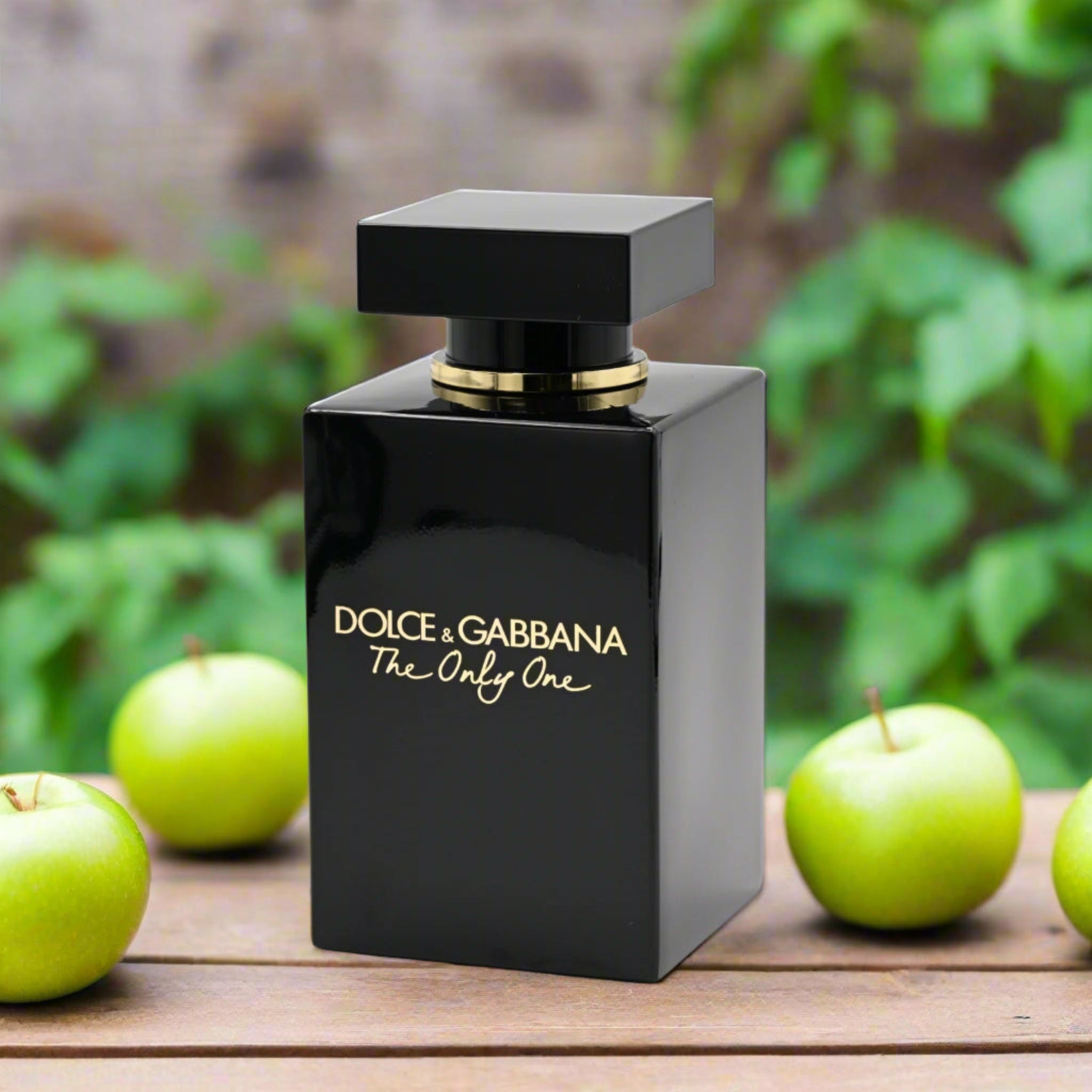 Black Dolce & Gabbana perfume bottle with green apples on a wooden surface