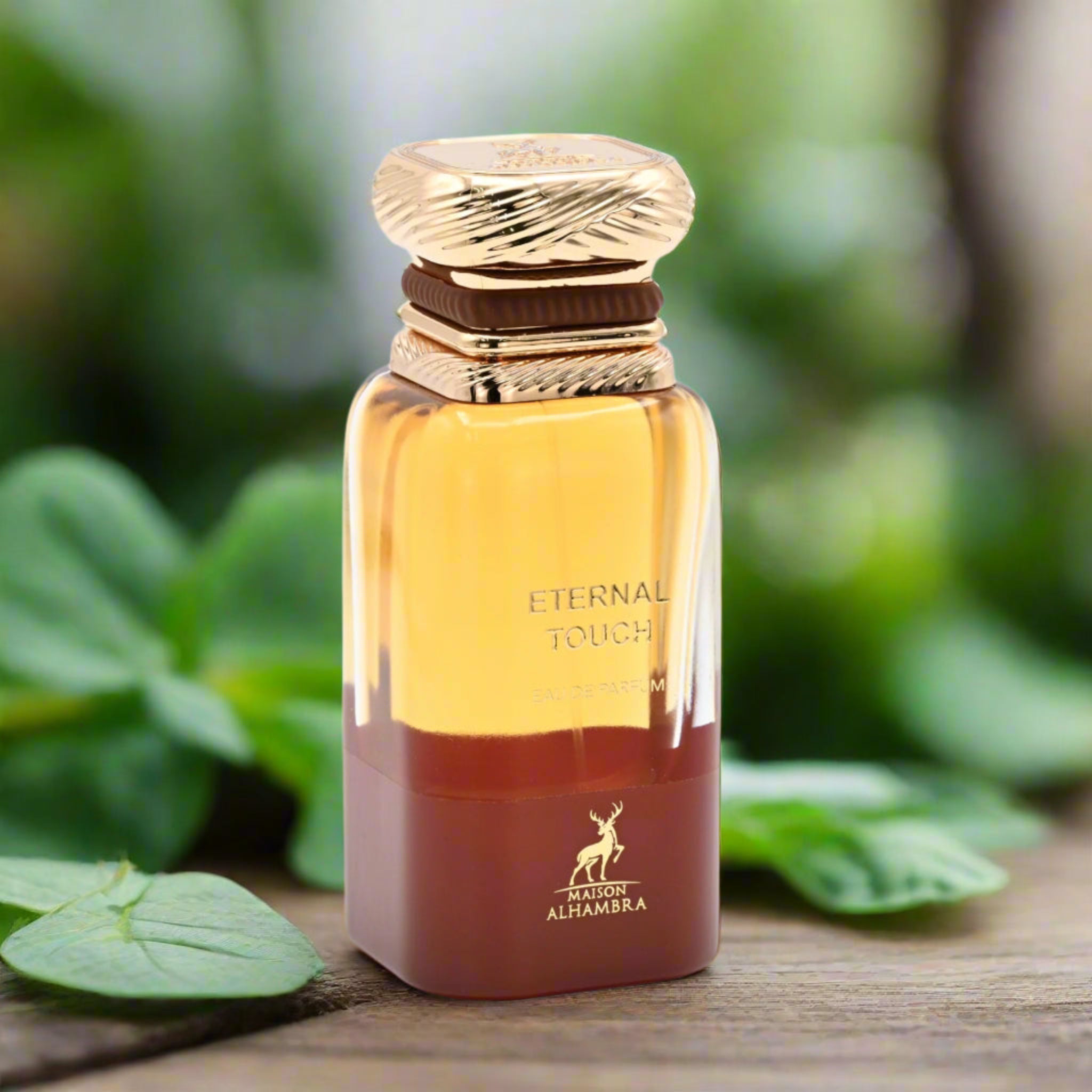 Perfume bottle labeled 'Eternal Touch' by Maison Alhambra on a wooden surface with green leaves in the background