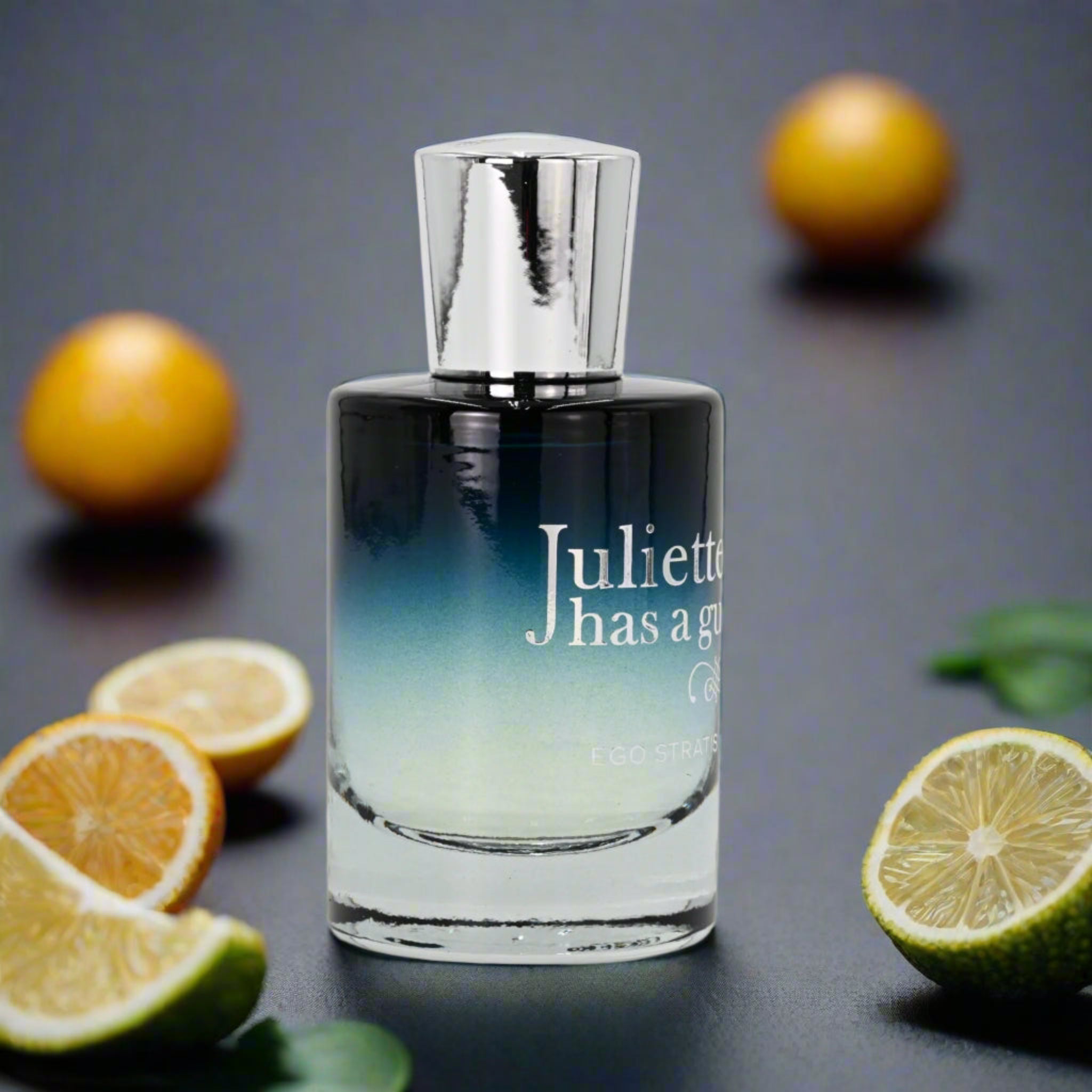 Perfume bottle with 'Juliette has a gun' branding surrounded by citrus fruits on a dark background