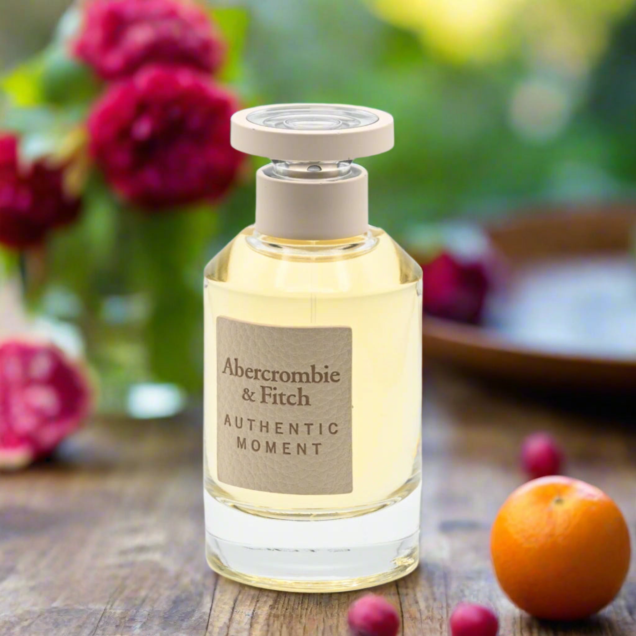 A bottle of Abercrombie & Fitch perfume on a wooden surface with flowers and fruits in the background