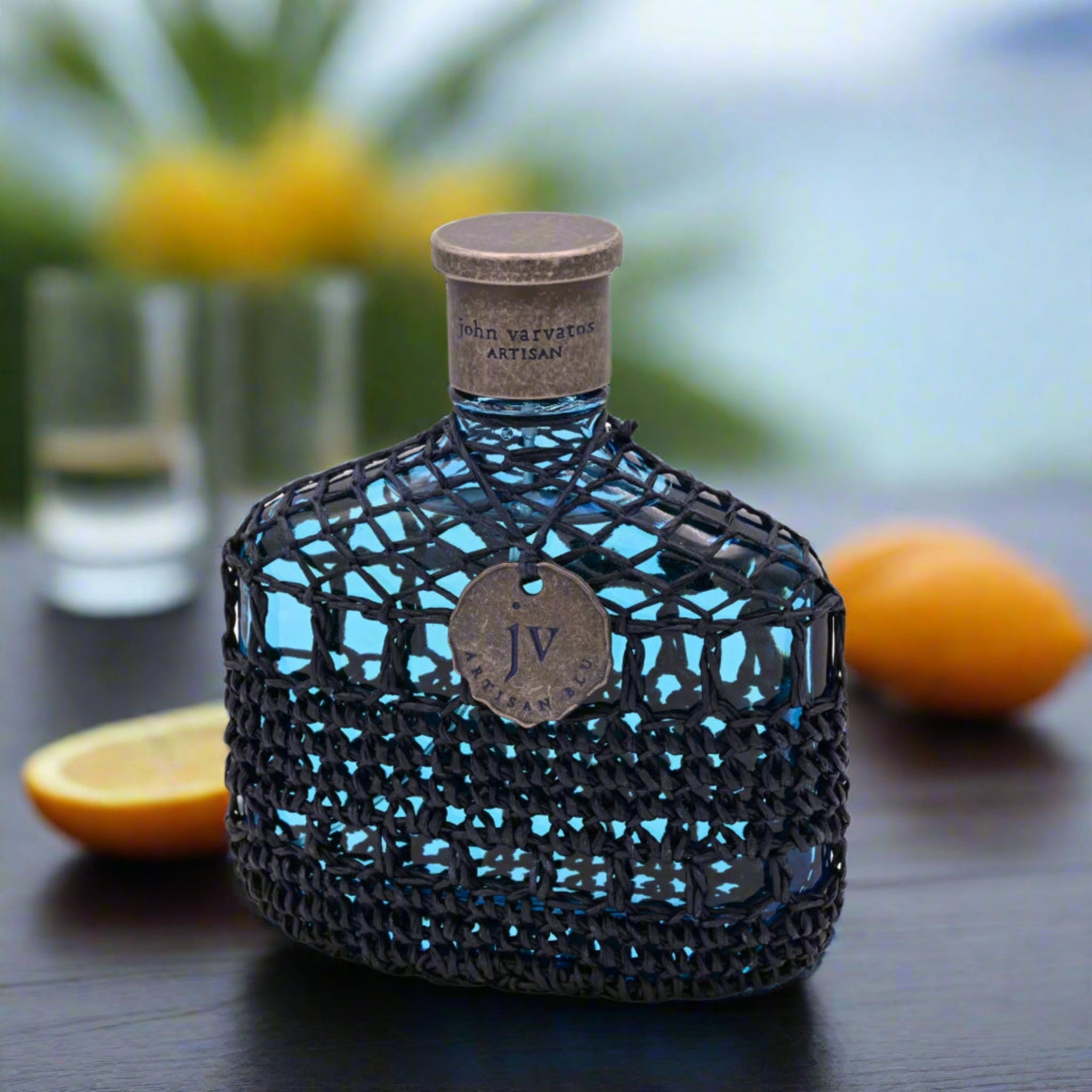 Glowing blue bottle with intricate design on a dark surface with oranges and a glass in the background