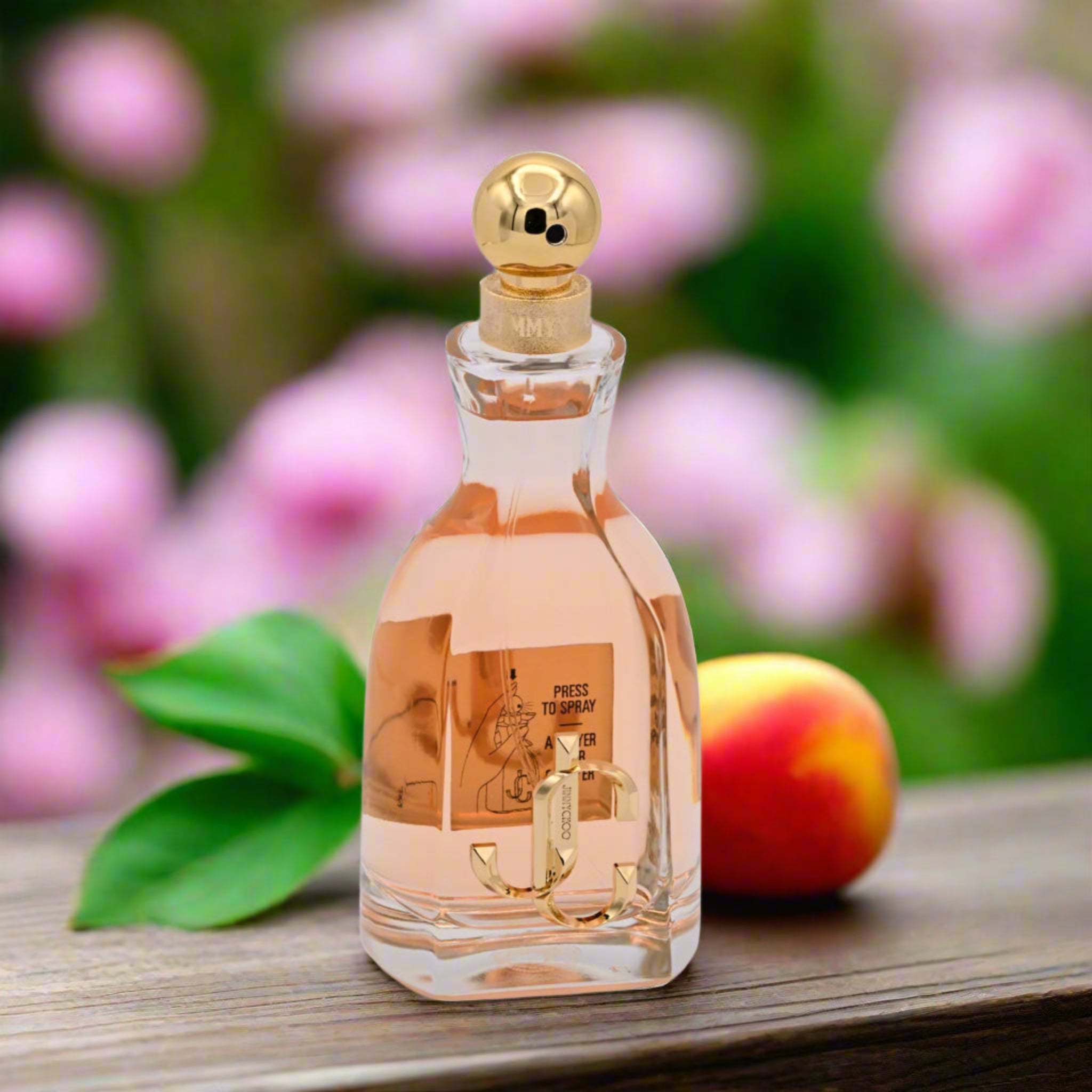 Perfume bottle with gold cap on a wooden surface with flowers and fruit in the background