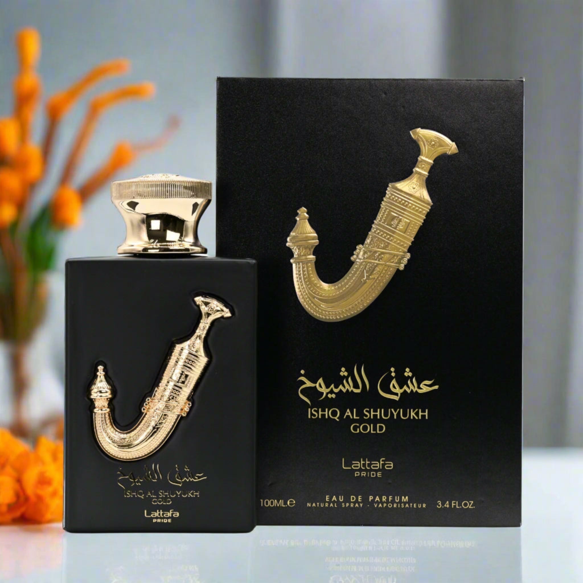 Lattafa Ishq Al Shuyukh Gold perfume bottle and packaging on a reflective surface with blurred orange flowers in the background.