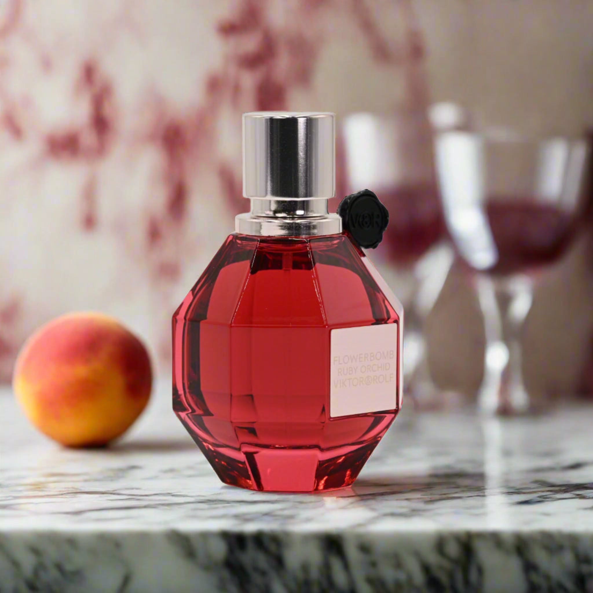 Red perfume bottle with silver cap on a marble surface with peach and glass in background