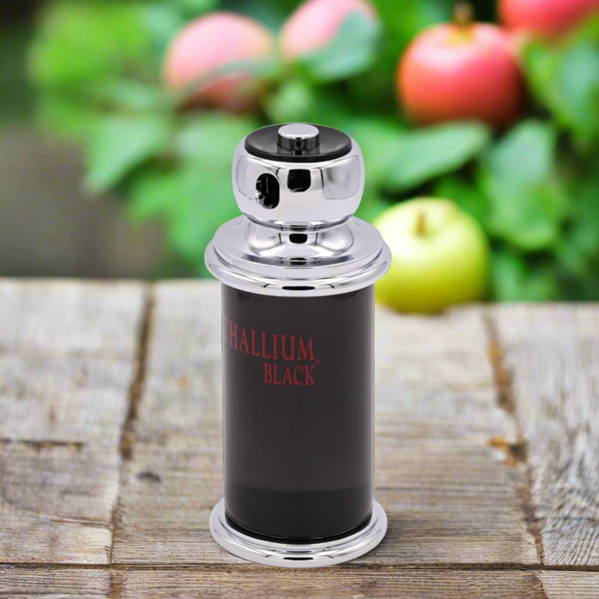 Perfume bottle labeled 'Phallium Black' on a wooden surface with blurred apples in the background