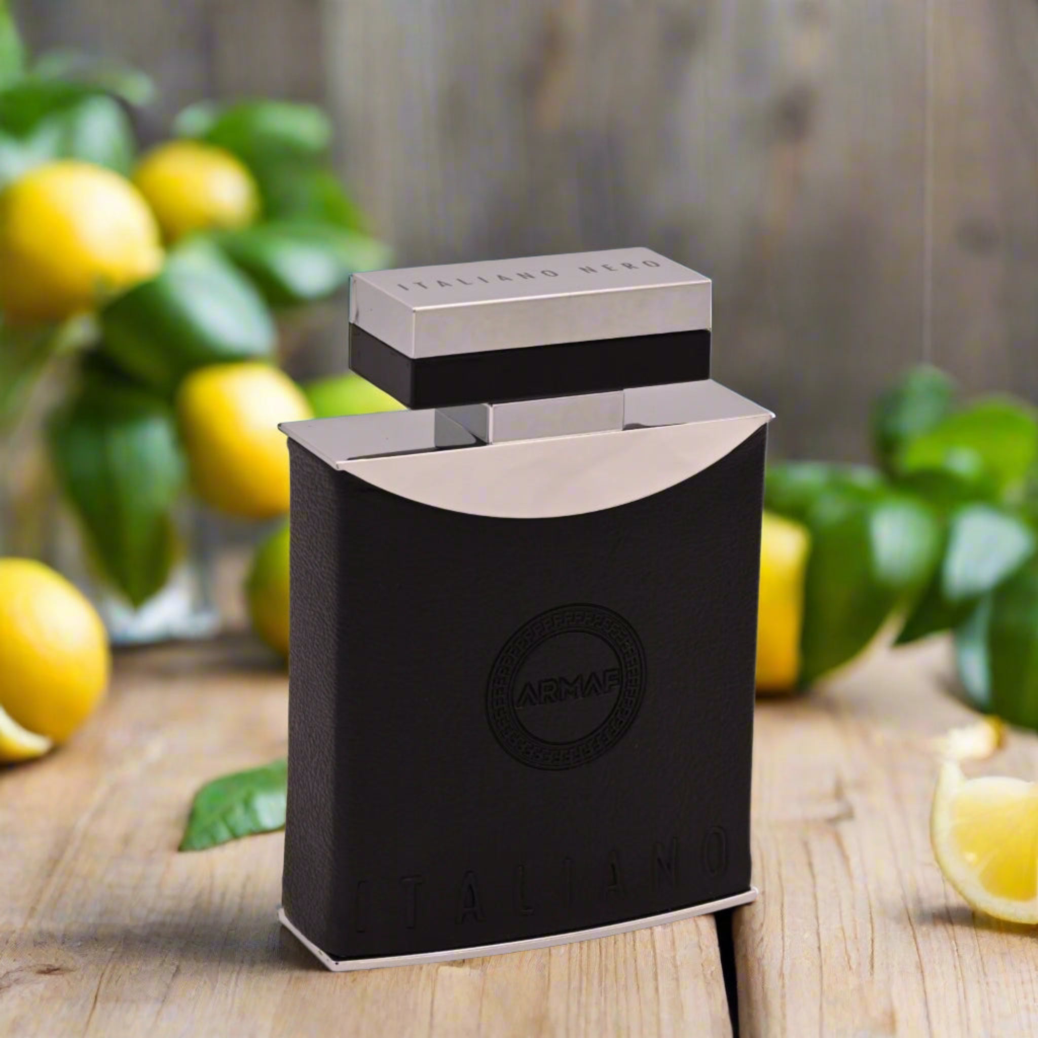 Black perfume bottle with silver cap on a wooden surface with lemons and greenery in the background