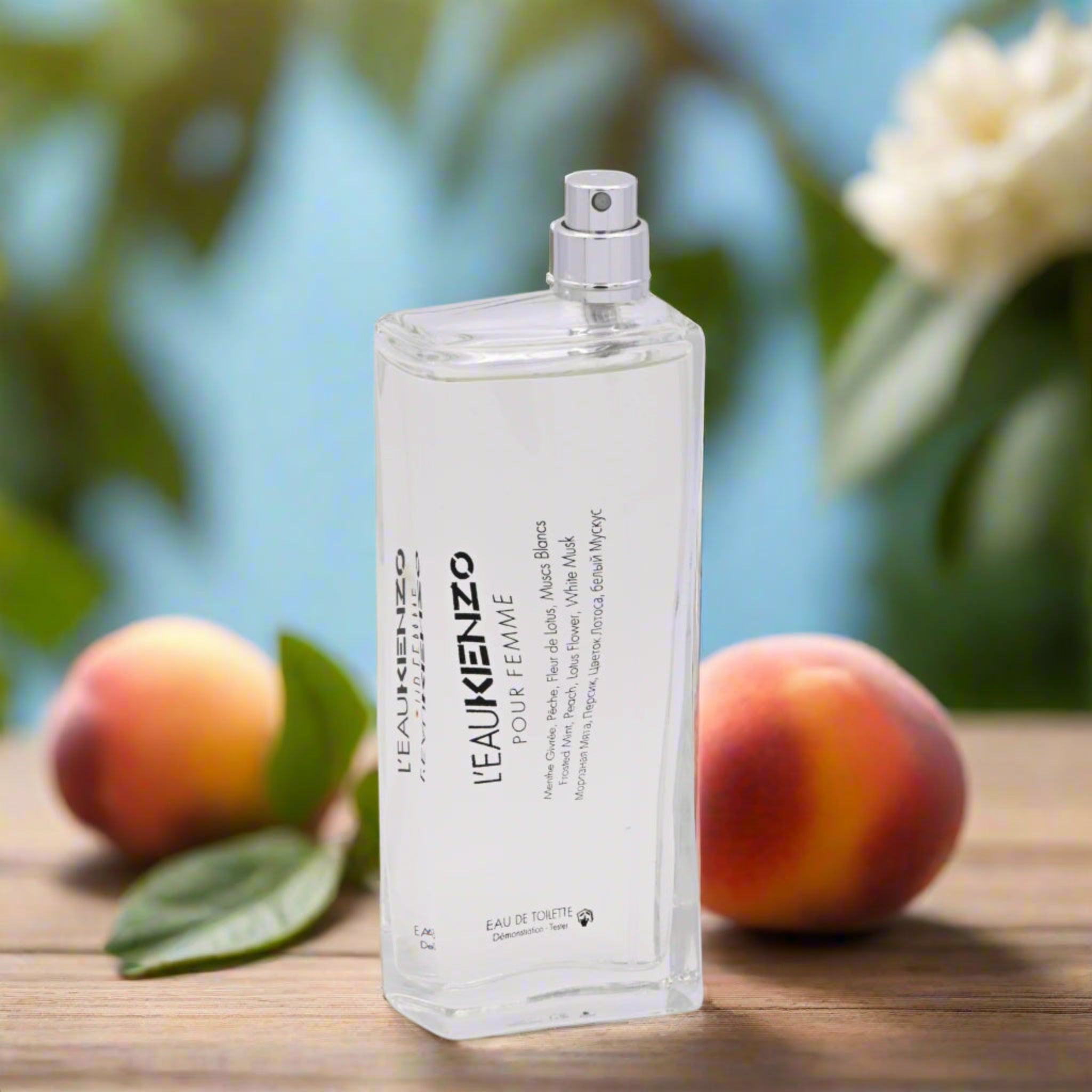 Kenzo perfume bottle with peaches and leaves on a wooden surface
