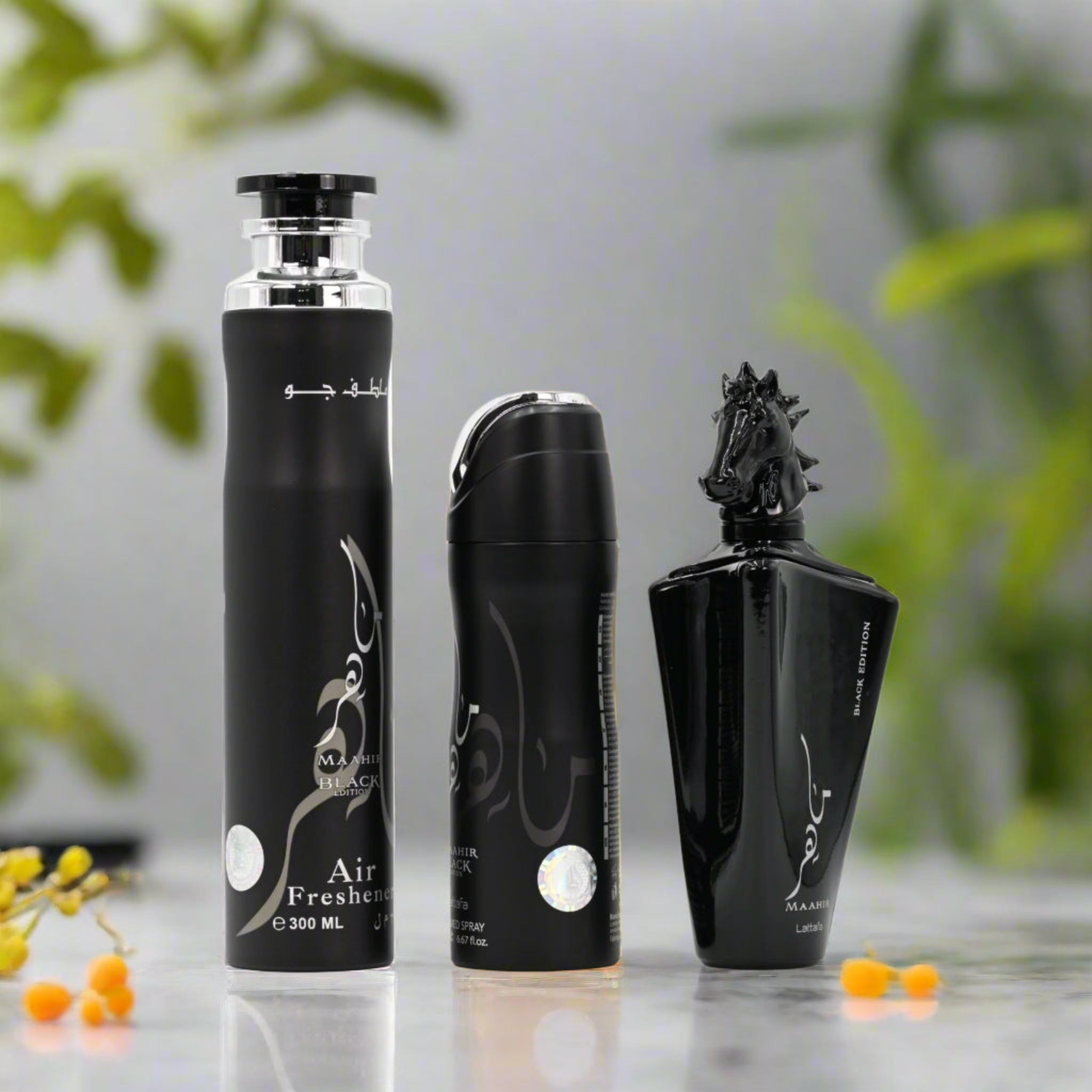 Three black perfume bottles on a reflective surface with a blurred green plant background.