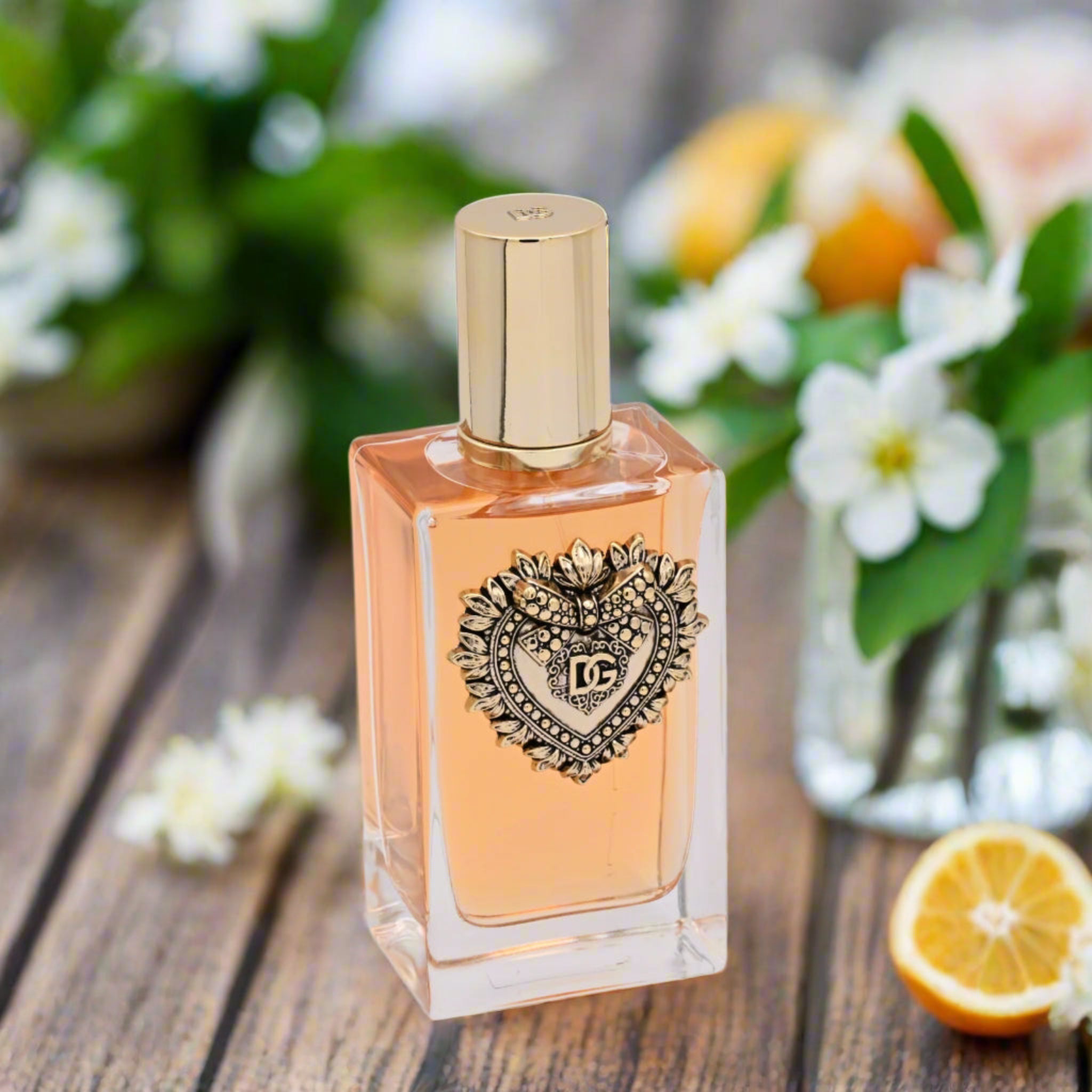 Perfume bottle with decorative heart emblem on a wooden surface with flowers and oranges in the background
