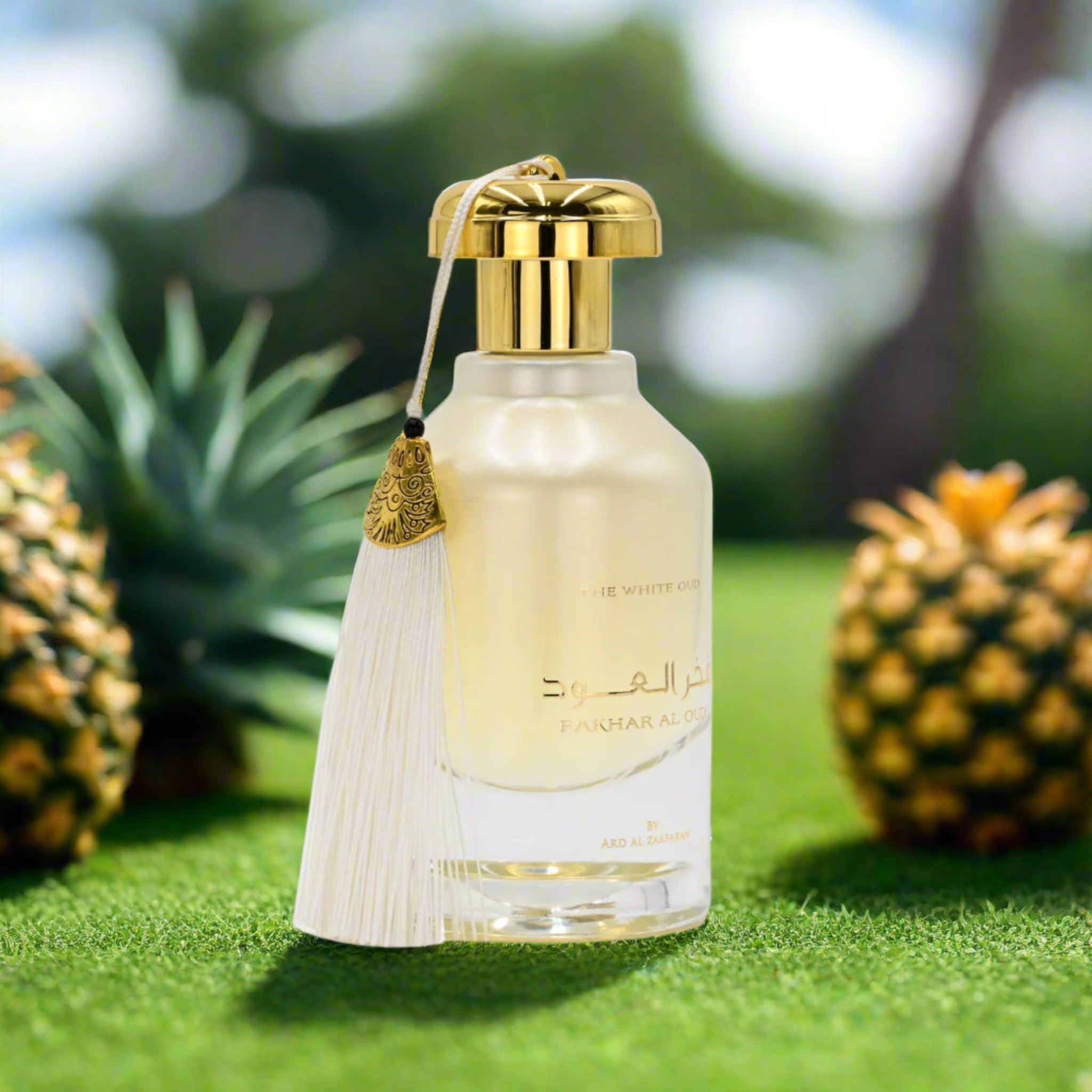 Perfume bottle with gold cap and tassel on grass with pineapples