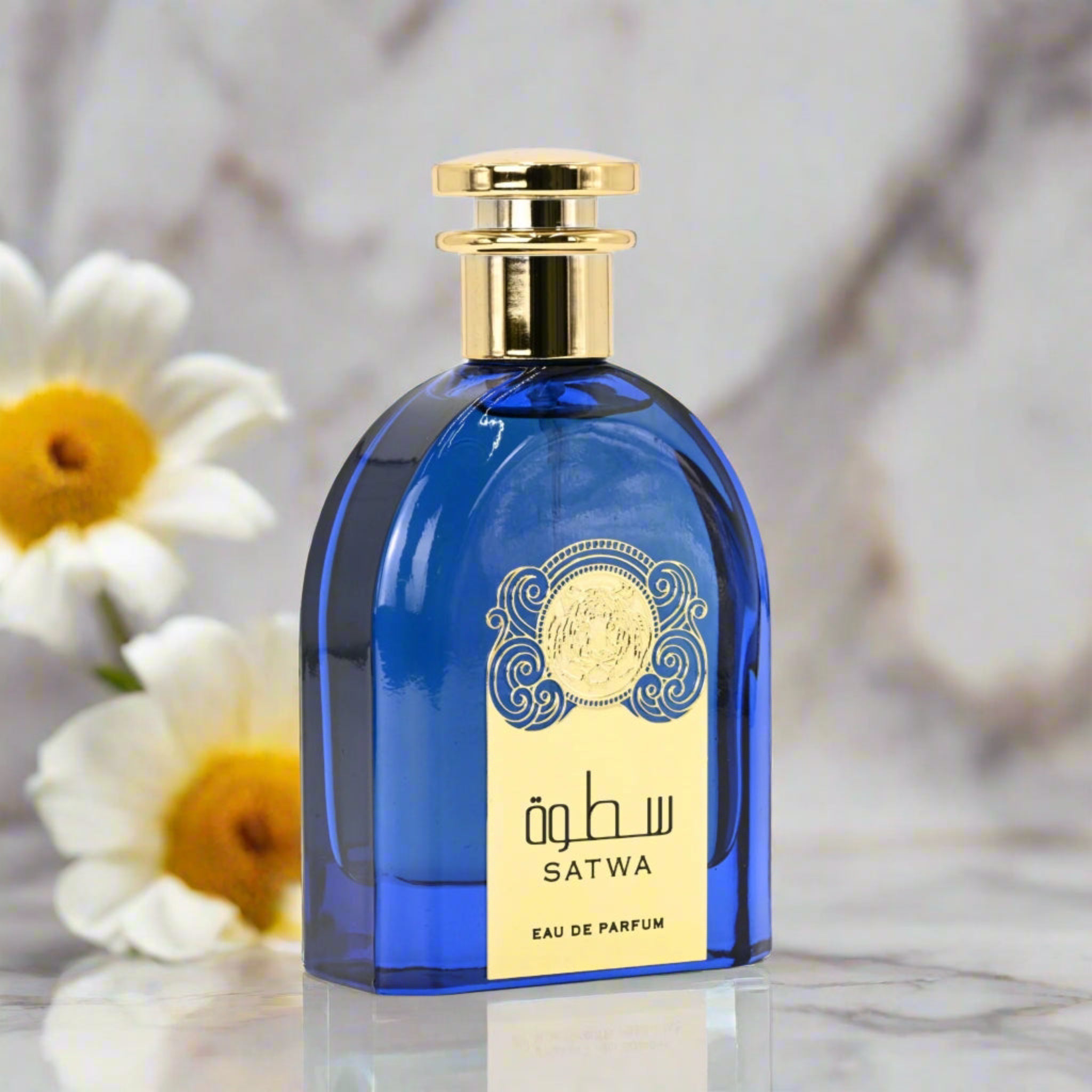 Blue Satwa perfume bottle with gold cap on a marble surface with flowers in the background