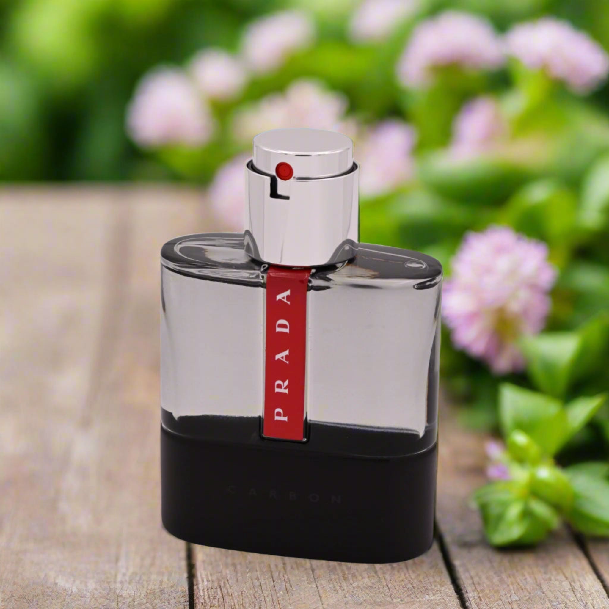 Prada perfume bottle on a wooden surface with flowers in the background