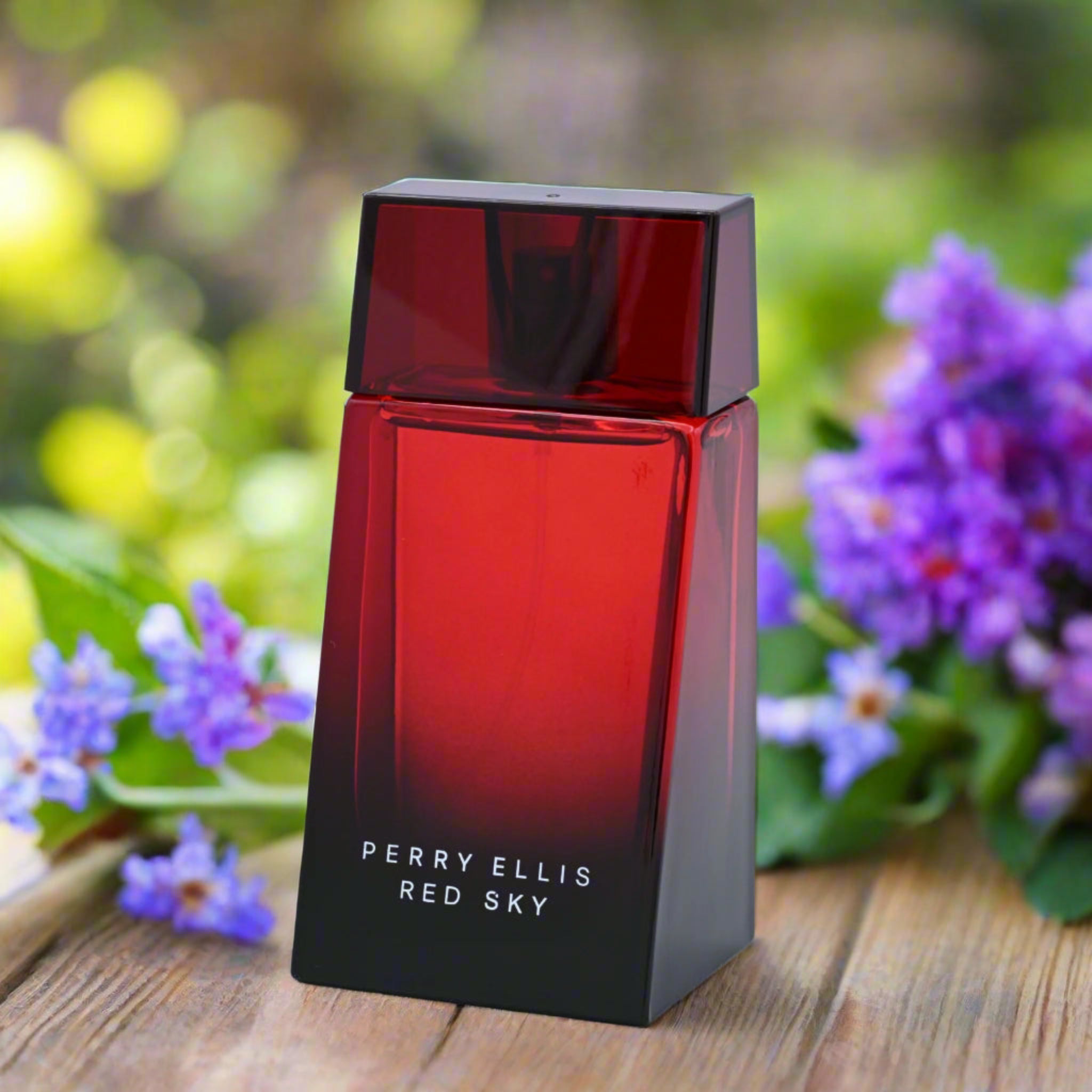 Perry Ellis Red Sky perfume bottle on a wooden surface with flowers in the background