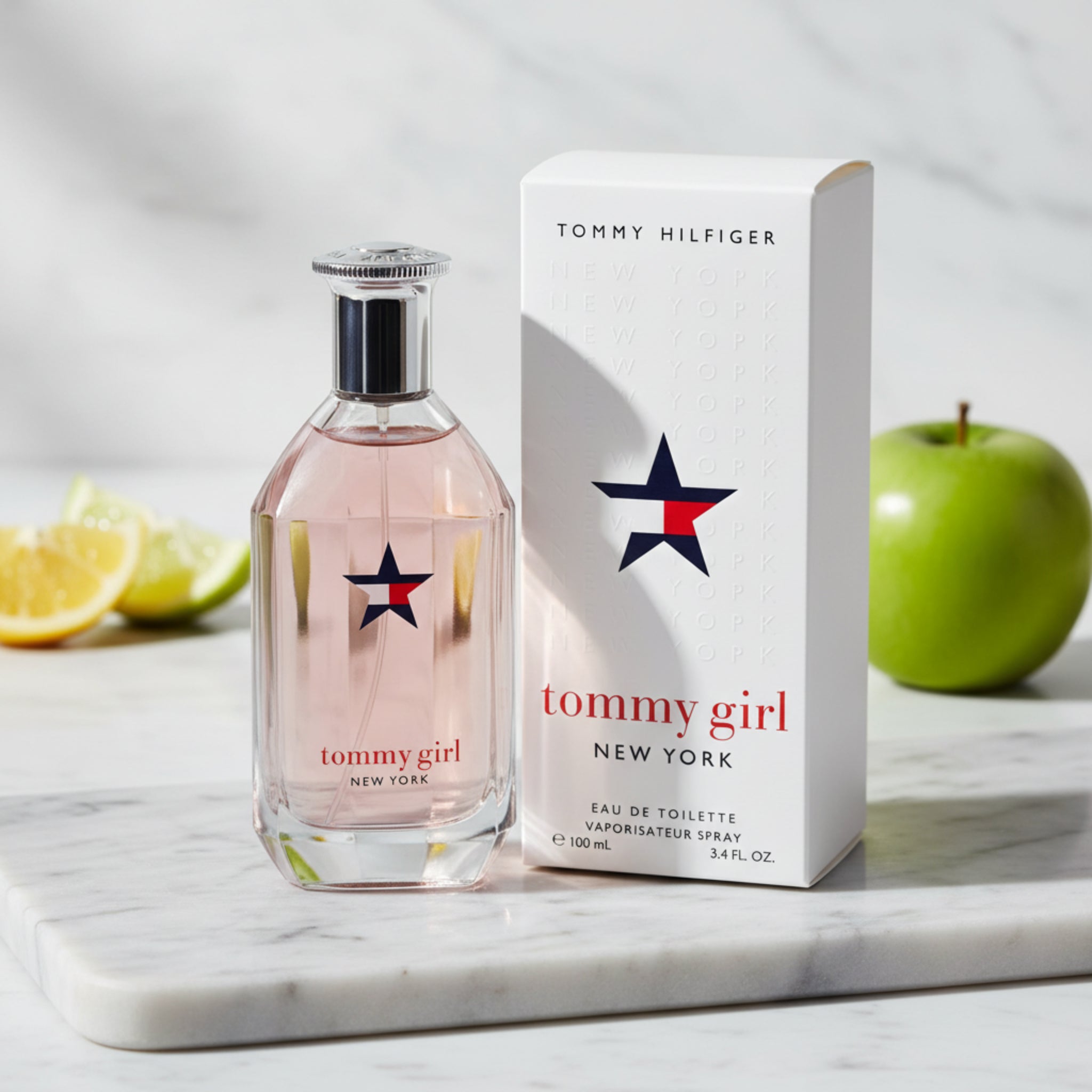 Tommy Girl perfume bottle and packaging on a marble surface with fruits in the background