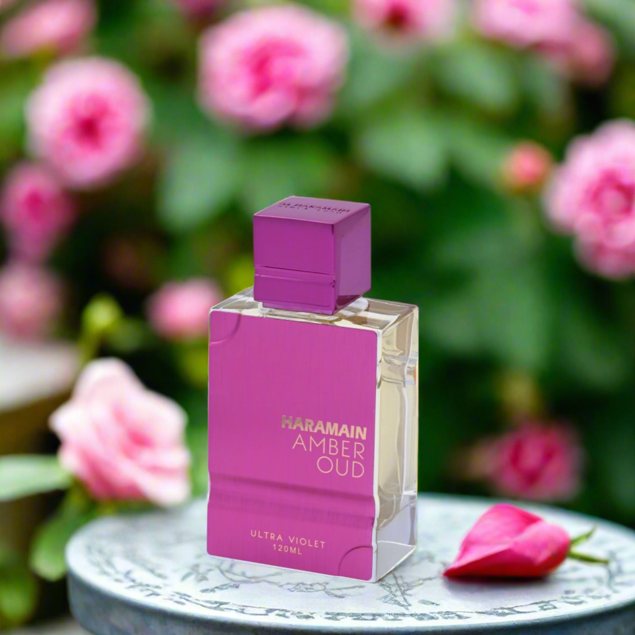 Haramain Amber Oud perfume bottle with pink packaging on a table with pink flowers in the background