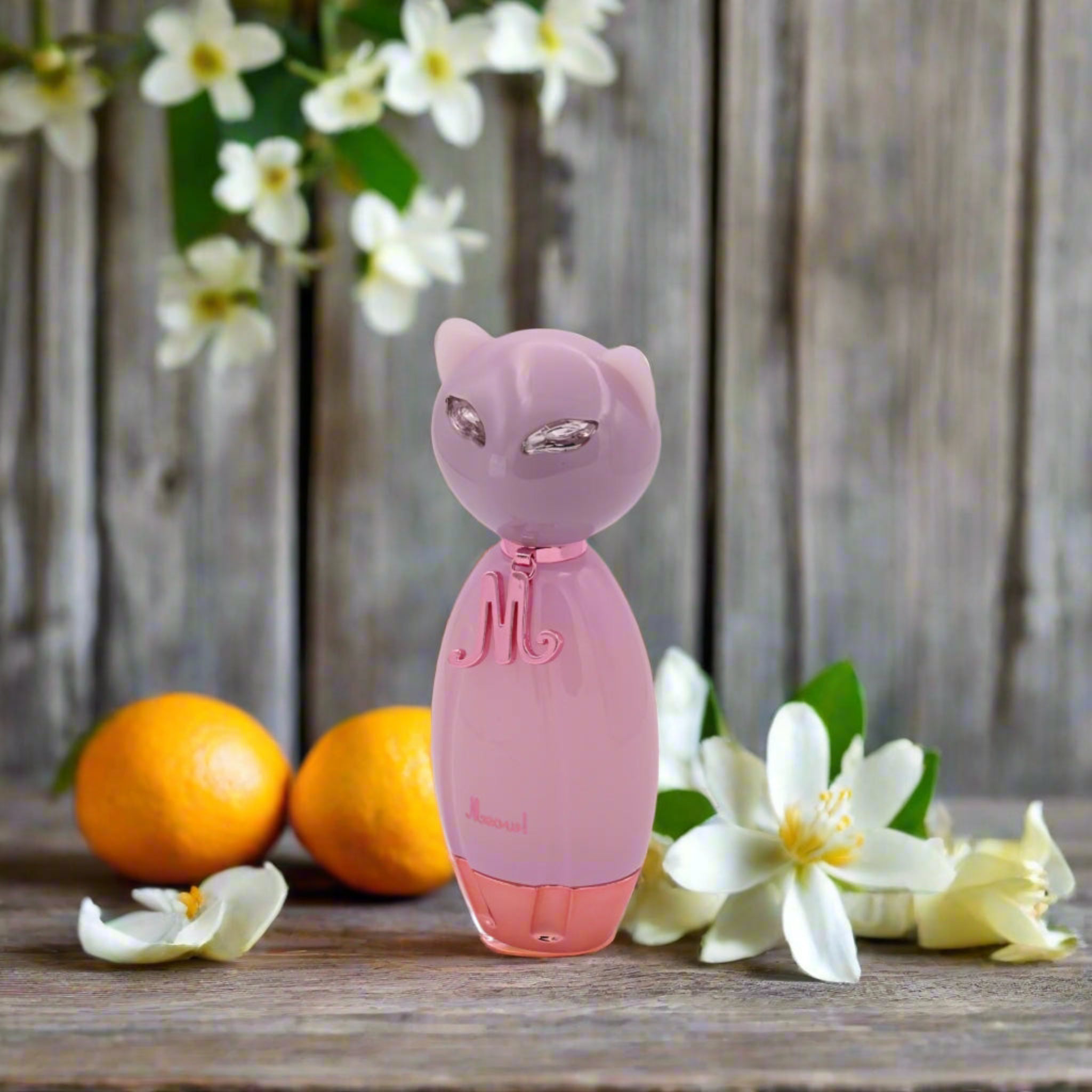 Pink cat-shaped perfume bottle with flowers and oranges on a wooden surface