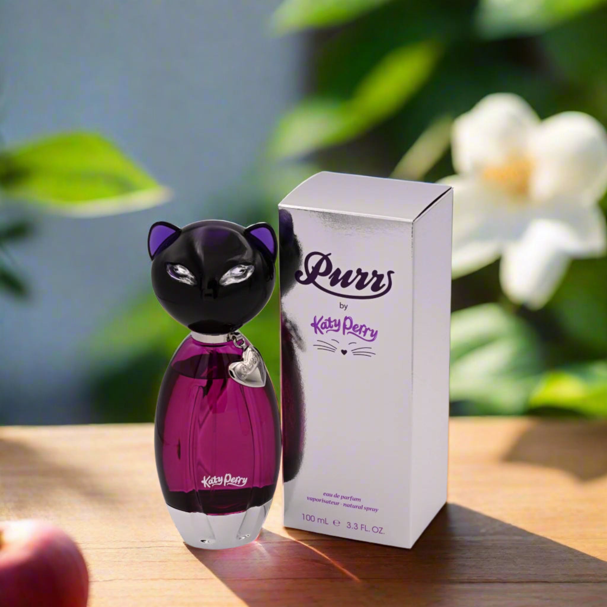 Katy Perry 'Purr' perfume bottle and packaging on a wooden surface with a blurred natural background
