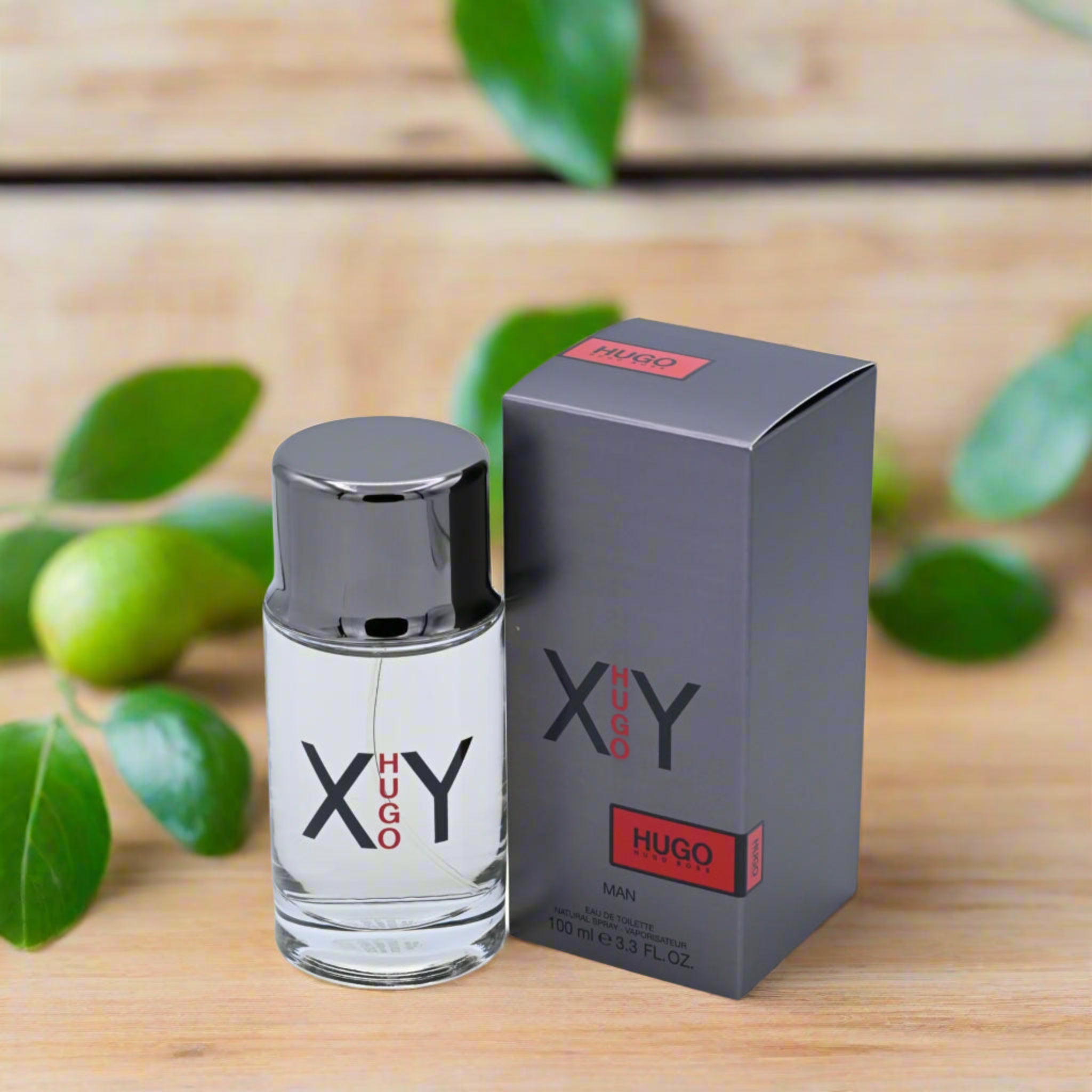 Hugo Boss XY perfume bottle and packaging on a wooden surface with green leaves.