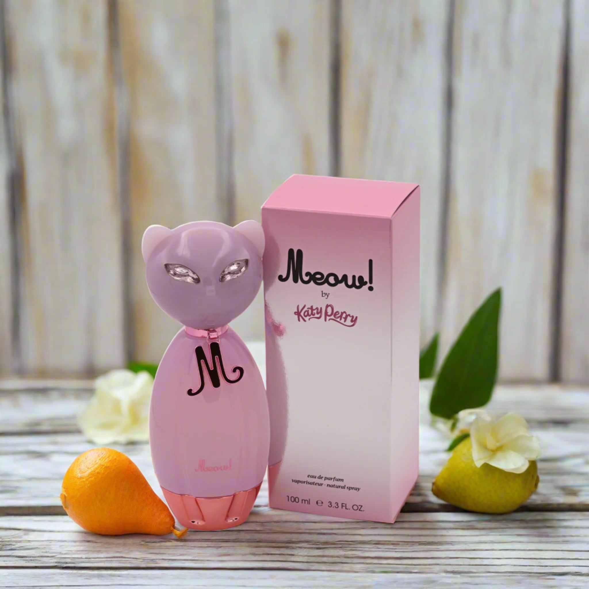 Pink cat-shaped perfume bottle and box labeled 'Meow! by Katy Perry' on a wooden surface with flowers.