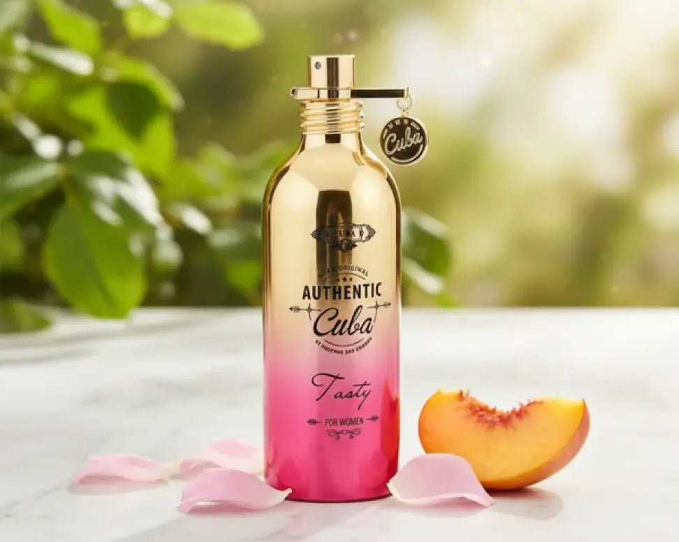 Cuba Tasty for Women perfume in a gold-to-pink ombre bottle with a Cuba charm, beside a peach slice and rose petals.