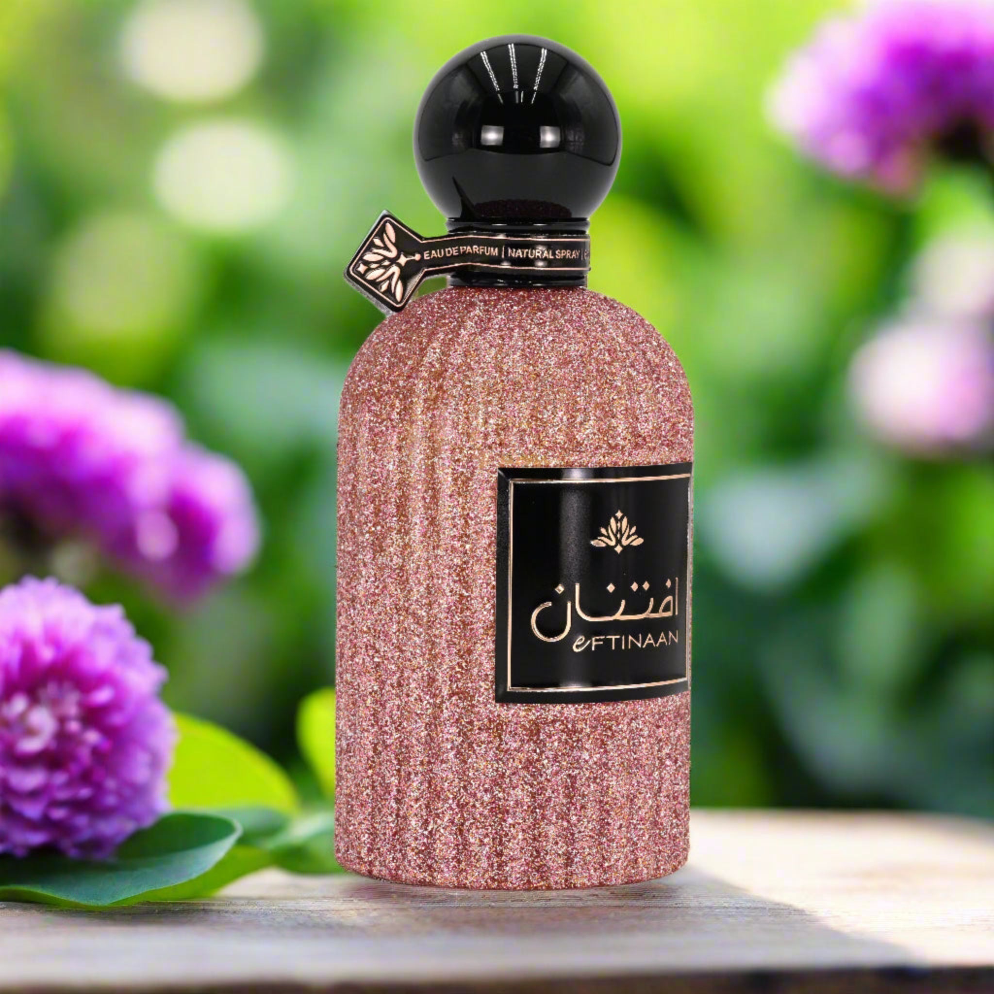 Perfume bottle with 'Oftinaan' branding on a wooden surface with purple flowers in the background