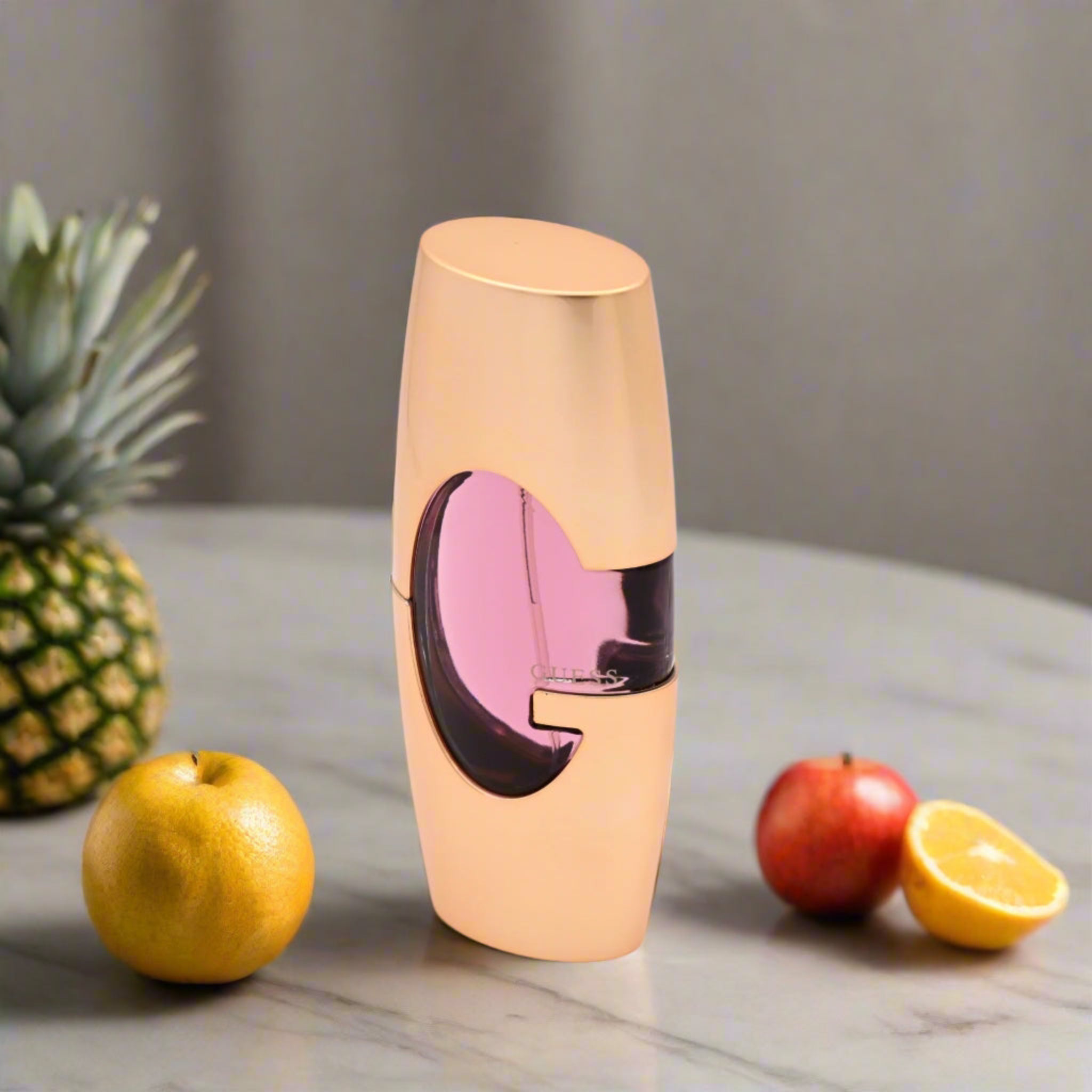 Guess Gold perfume bottle with pink and black design on a marble surface with fruits