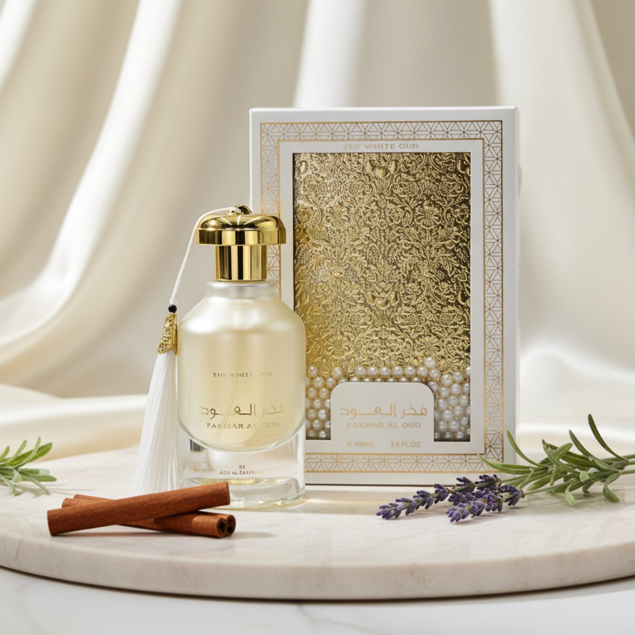 Perfume bottle with gold cap and tassel next to its decorative box on a white background